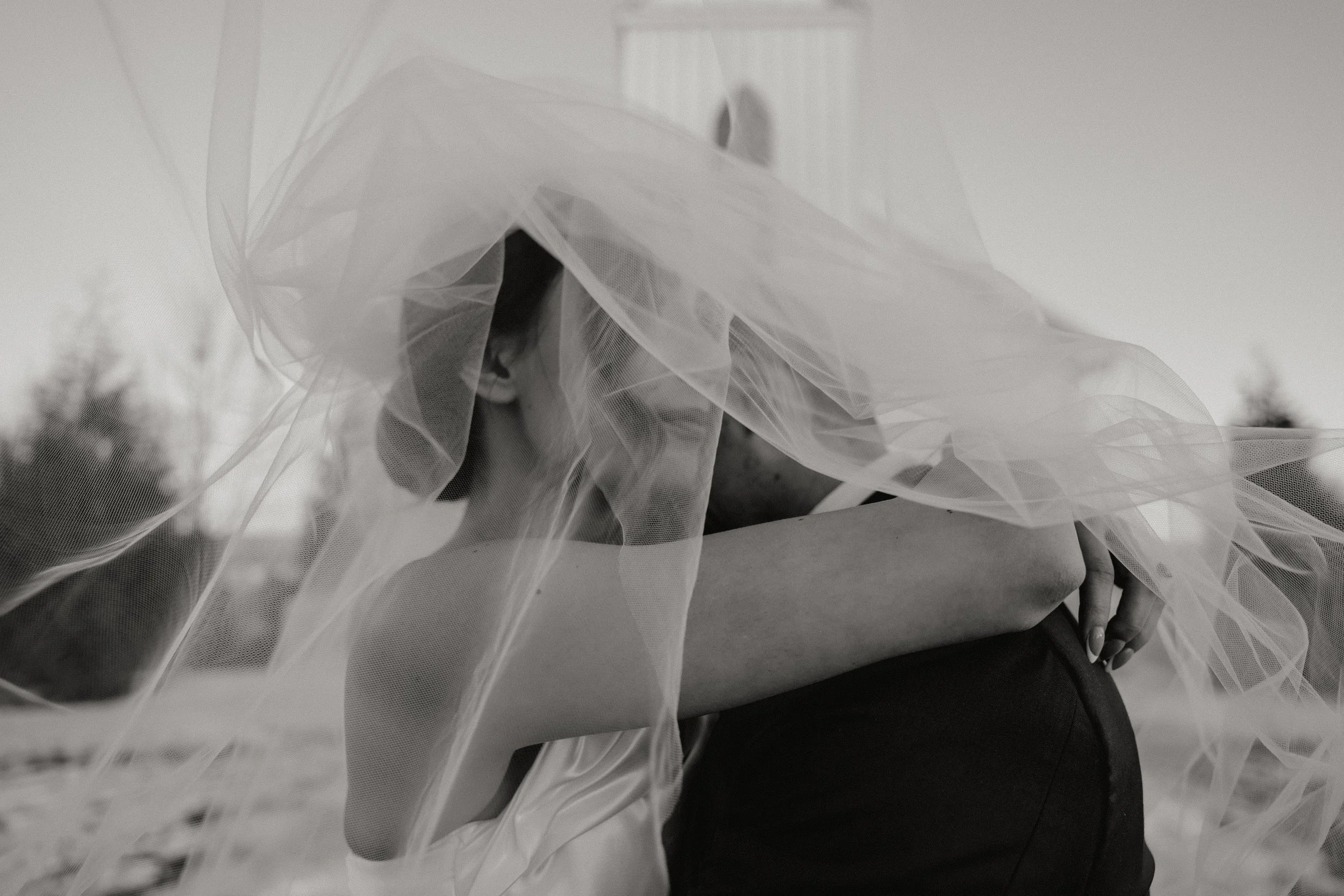 A woman wearing a wedding dress and veil, hugging a man outdoors on their wedding day in Somerville, New Jersey photographed by Dominique Paulette Photography