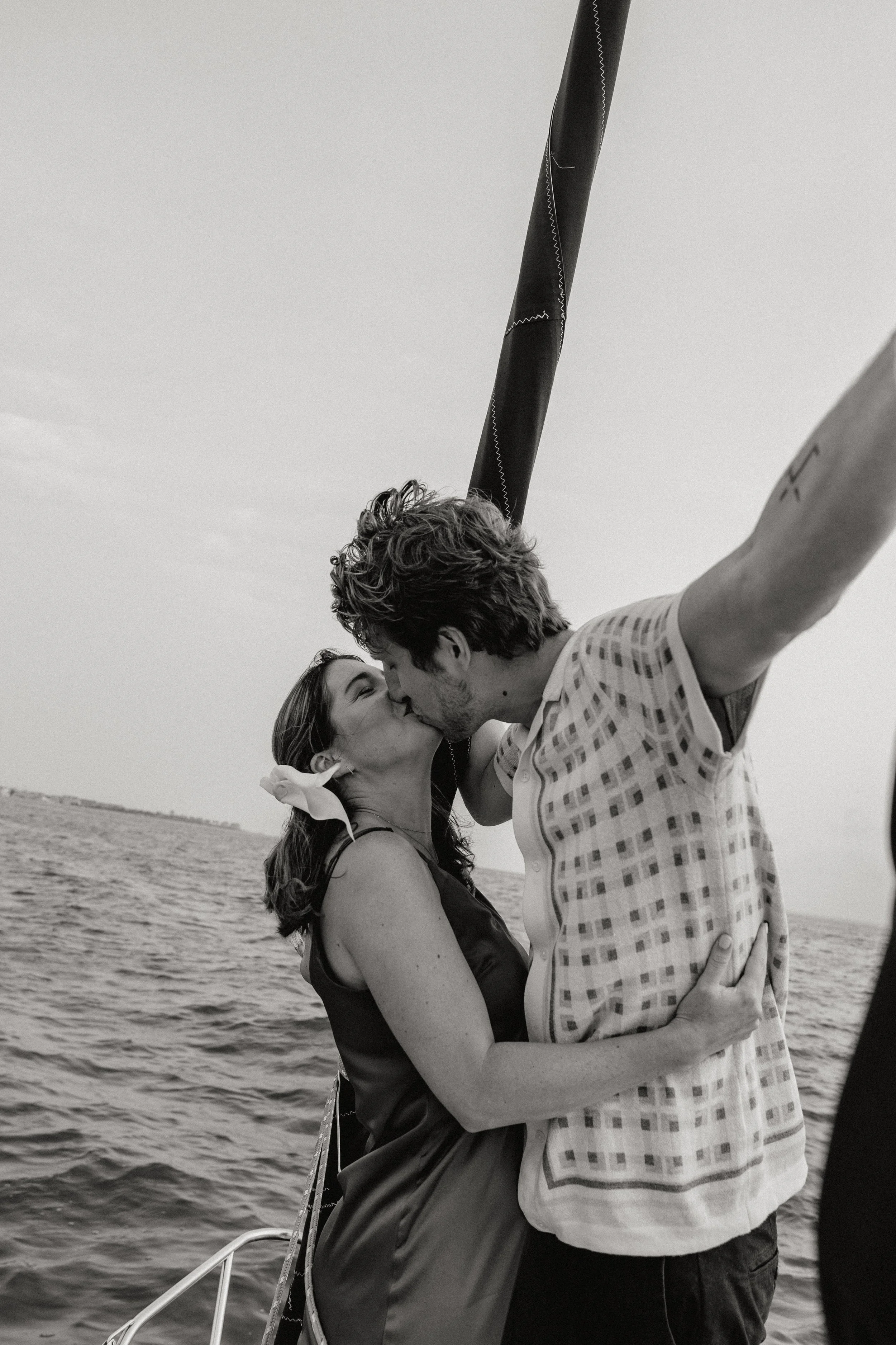 A couple kissing on a boat near the ocean, with a flagpole overhead, in black and white in New Jersey, photographed by Dominique Paulette Photography