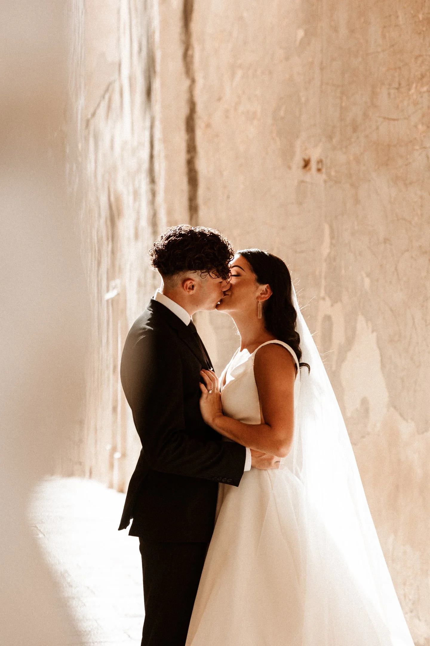 A bride and groom kissing in front of a textured wall during their wedding in Malta, photographed by Dominique Paulette Photography