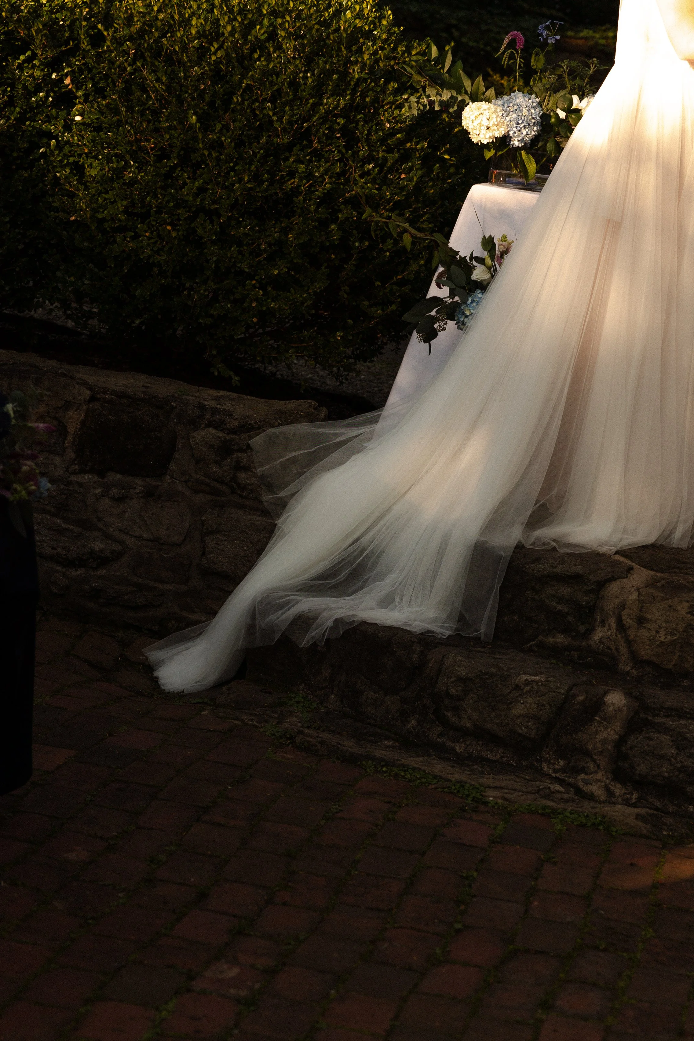 Part of a wedding dress with a long train on cobblestone ground near greenery and flowers in Somerville, New Jersey photographed by Dominique Paulette Photography