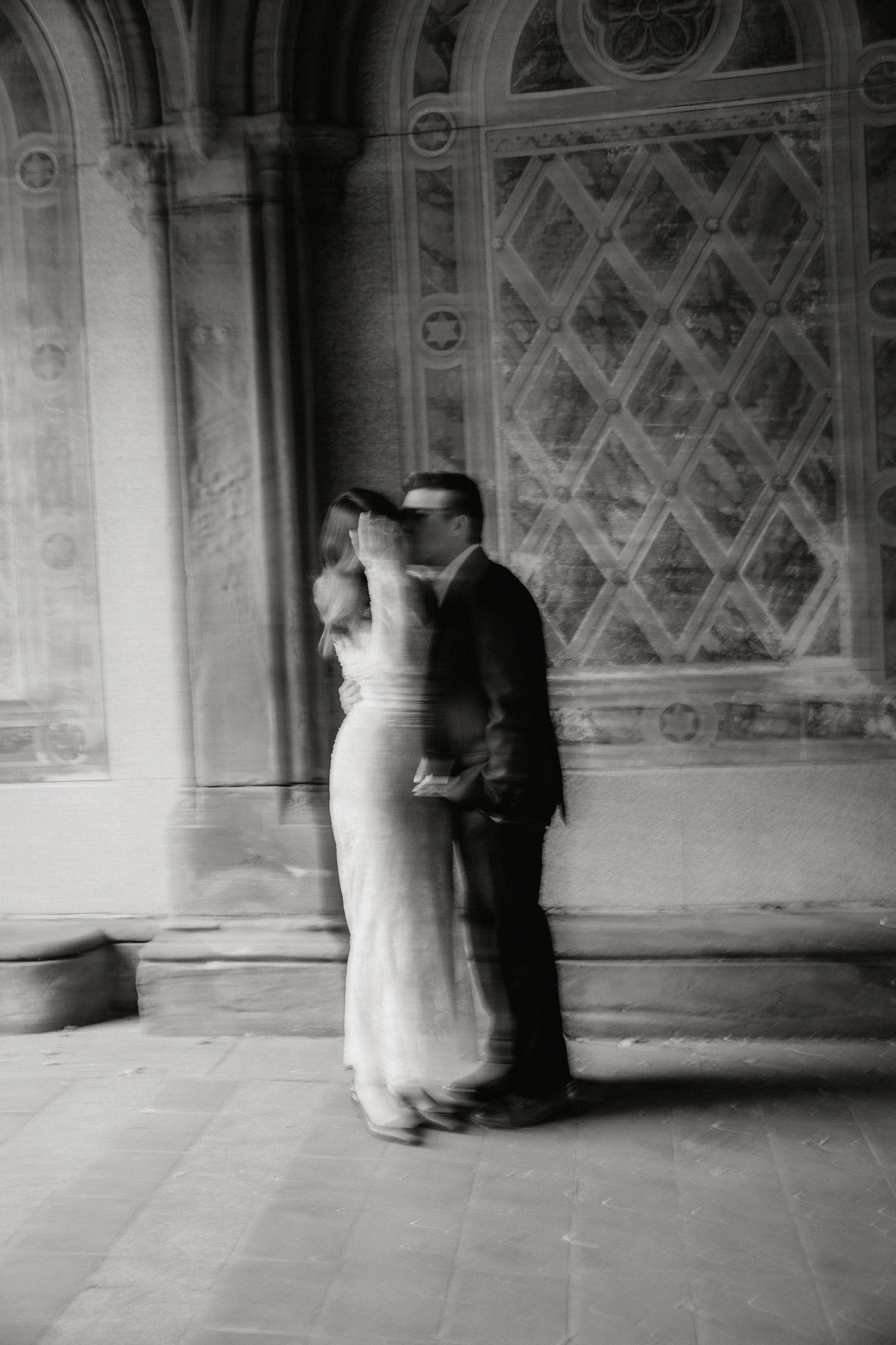 A black and white photo of a couple in wedding attire sharing a kiss, standing in front of an ornate building wall for their wedding in Somerville, New Jersey photographed by Dominique Paulette Photography