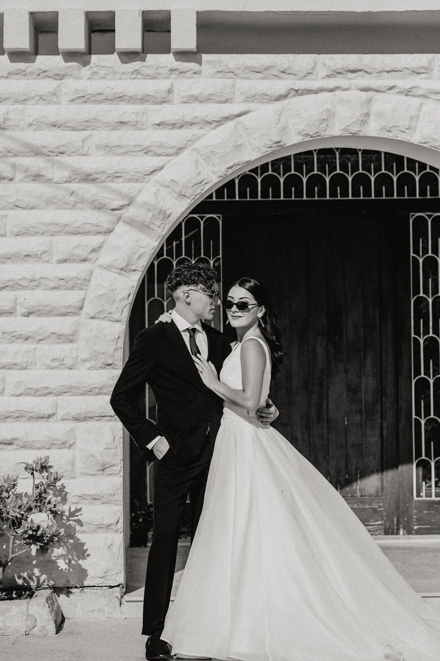 Black and white photo of a couple in wedding attire posing under a stone archway in Malta photographed by Dominique Paulette Photography