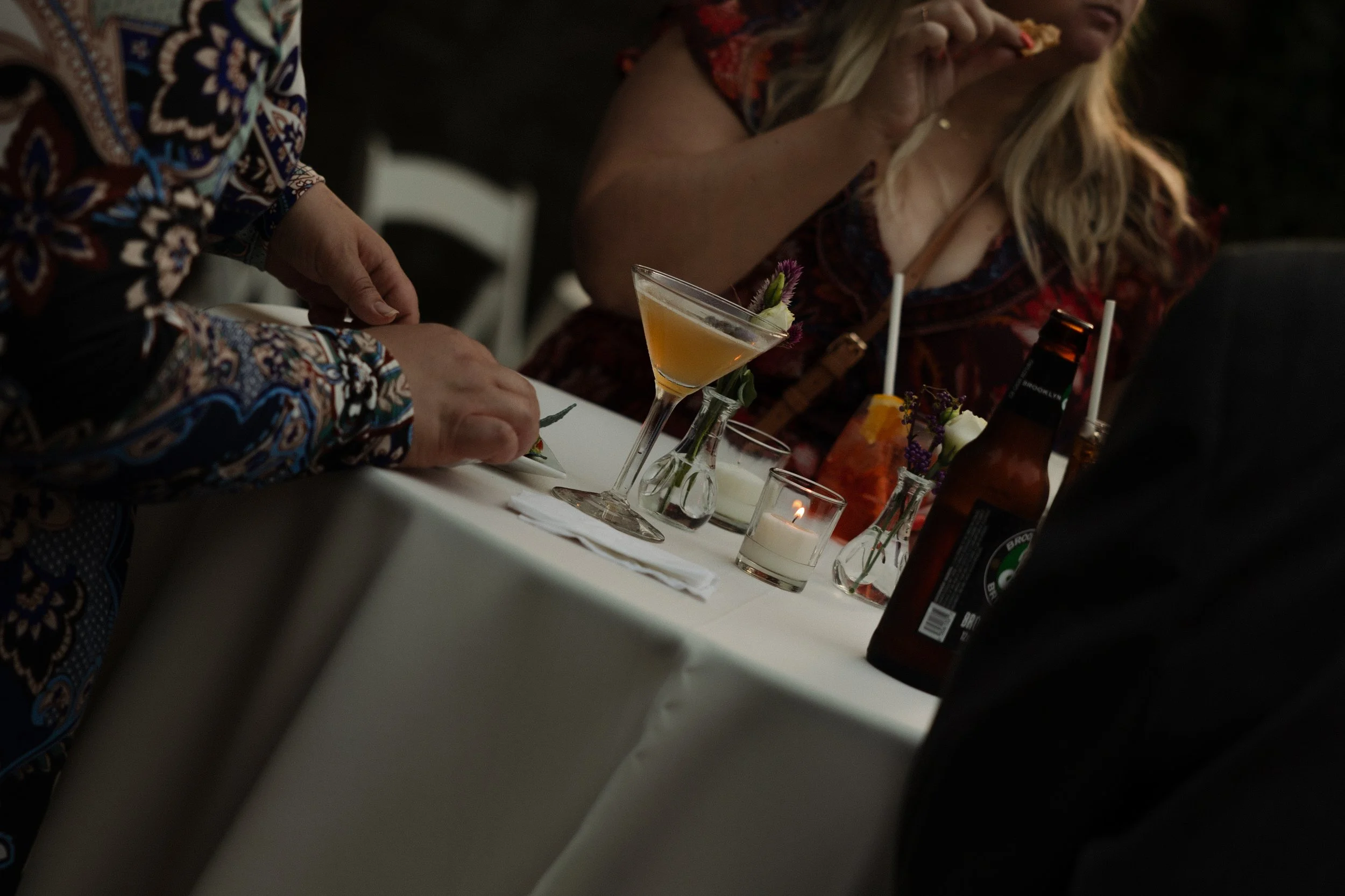 People gathered around a table at a social event, with drinks, candles, and small floral arrangements on the table.