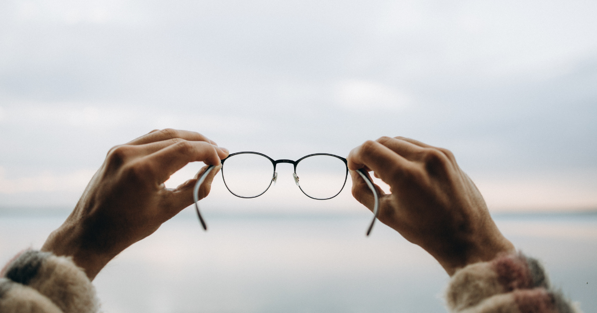 Person holding glasses in front of a cloudy sky over water