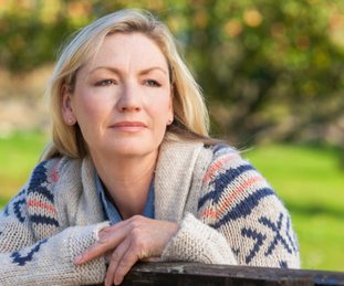 A woman with blond hair and sweater outside, looking off into the distance