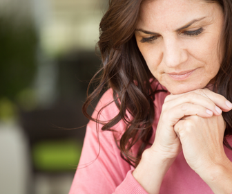 A middle aged woman with brown hair looking downward with a pensive expression