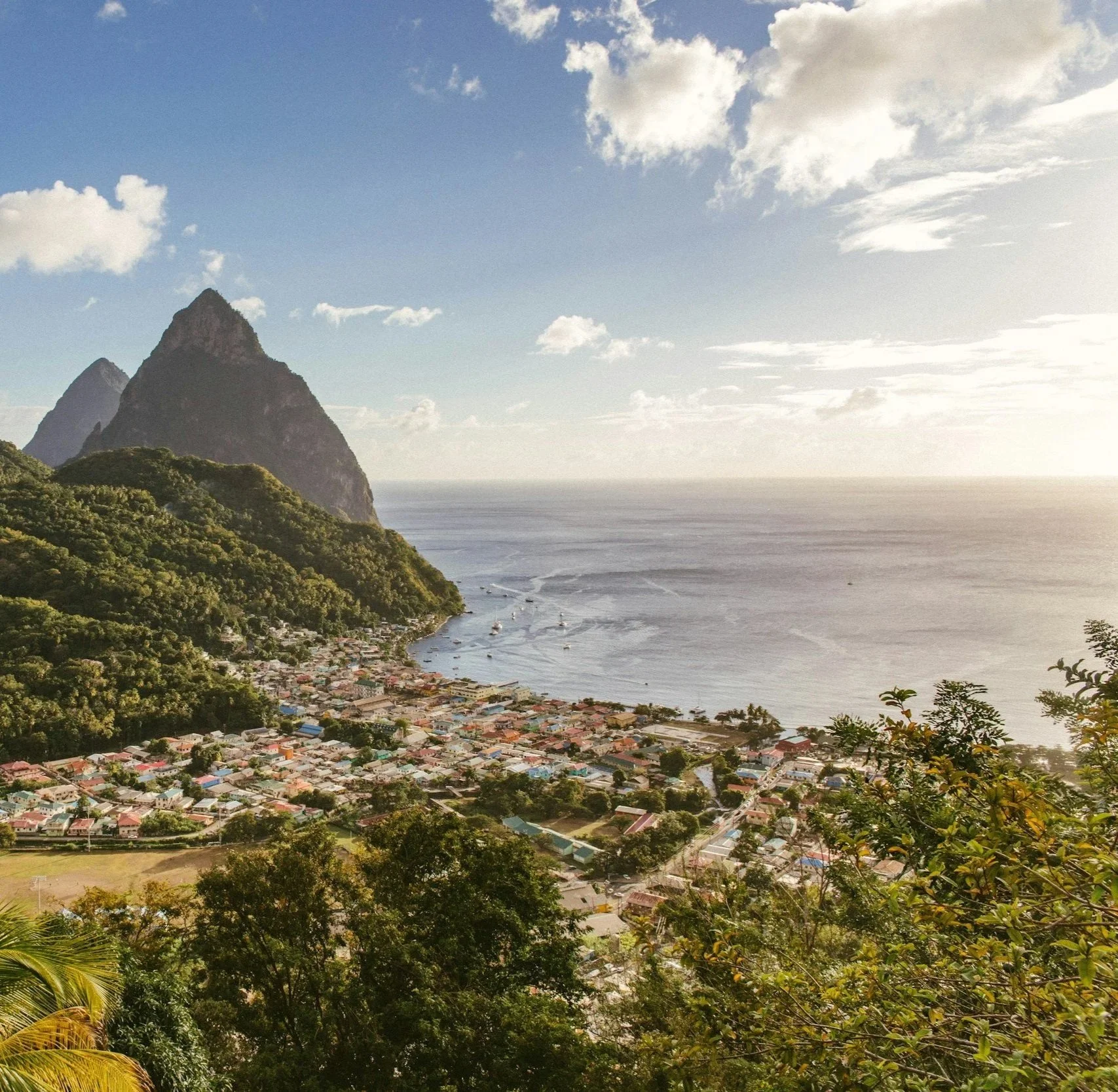 Panoramic view of the Pitons and Soufrière on St Lucia, with lush green mountains, colourful coastal buildings and the Caribbean Sea, a highlight of a Caribbean sailing holiday
