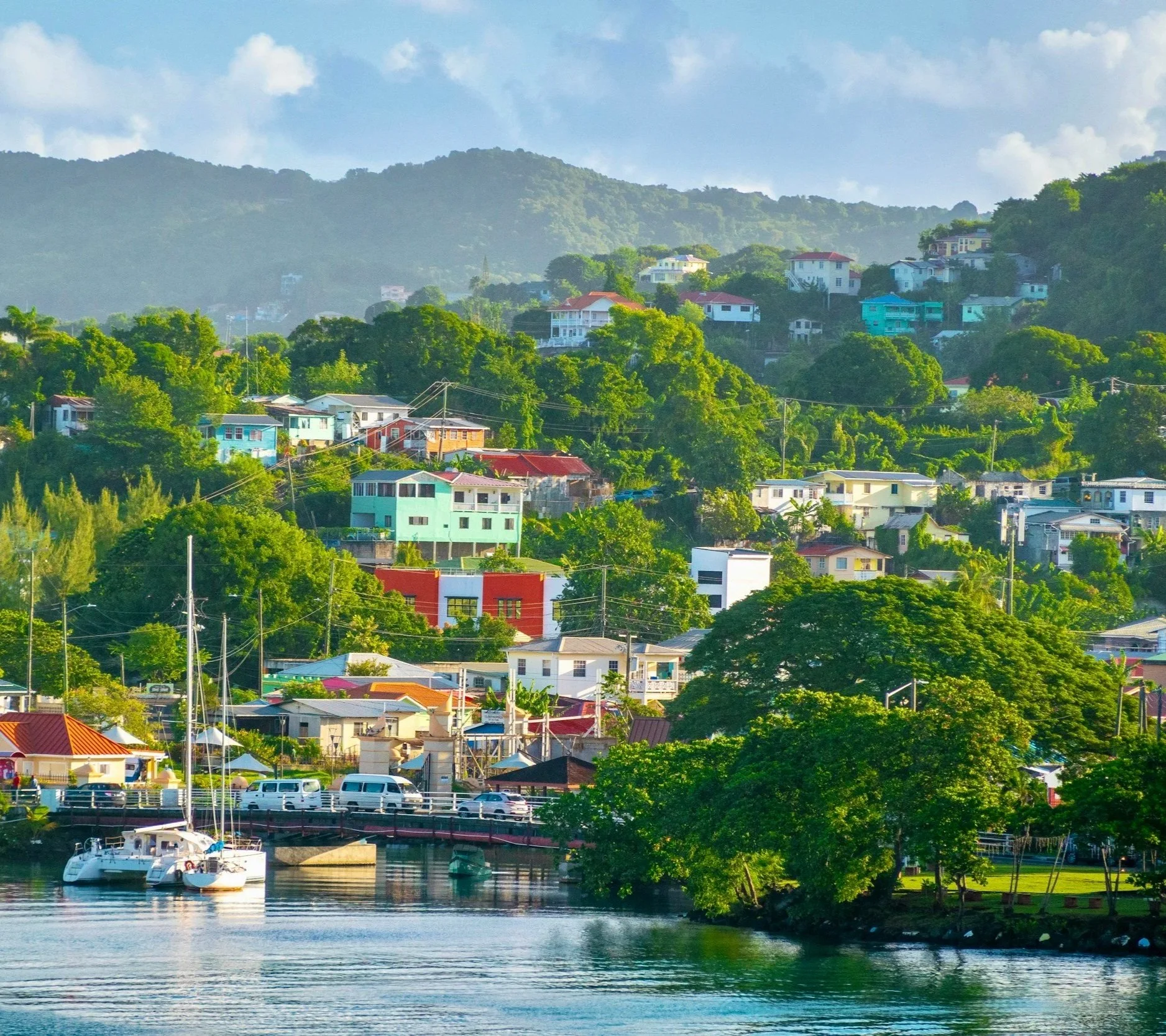 Colourful Caribbean waterfront town with small boats moored in a sheltered harbour beneath lush green hills, an inviting stop on a Caribbean sailing holiday