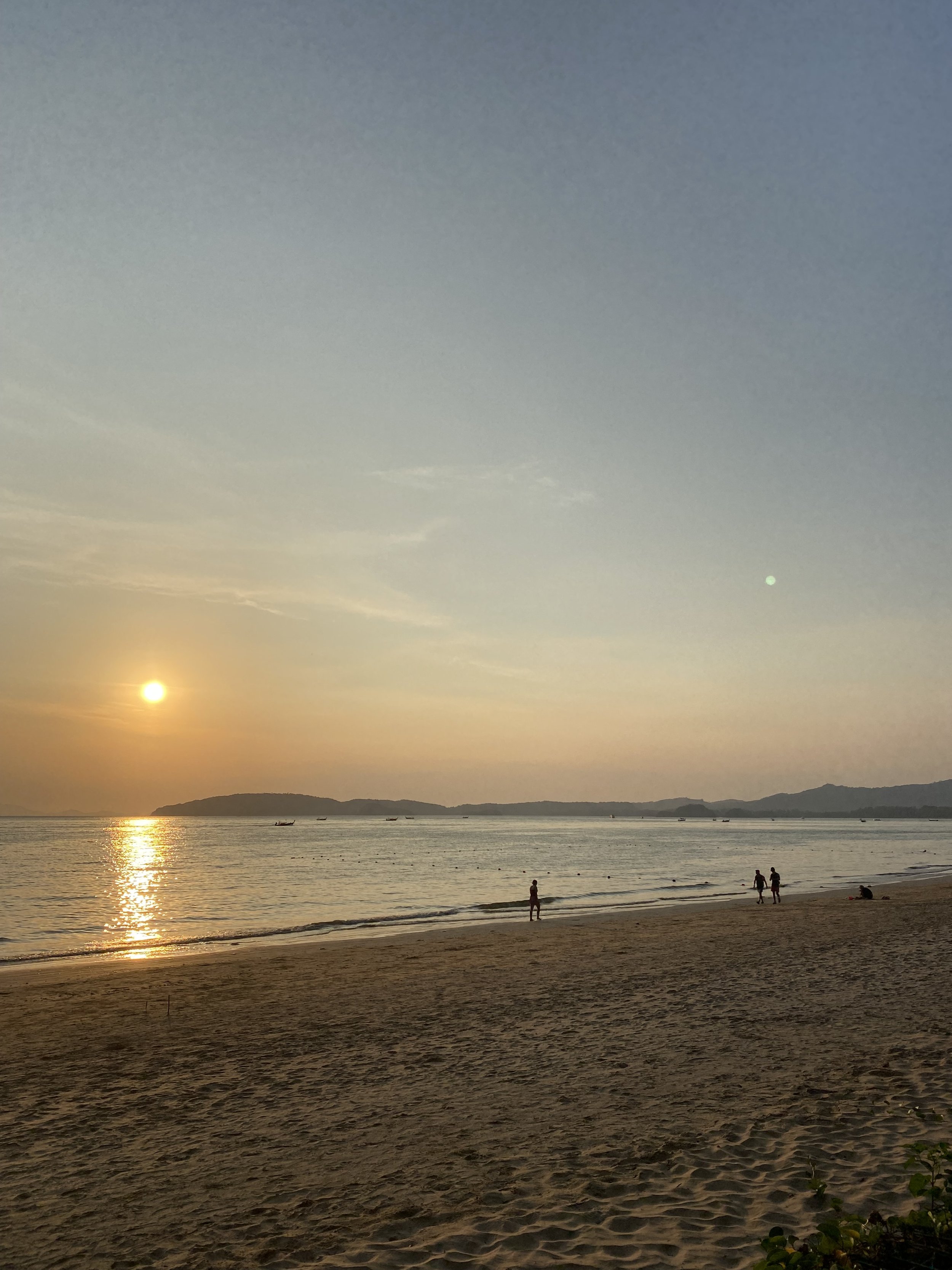 Sunset over a beach in Krabi, Thailand, with distant mountains and a peaceful shoreline