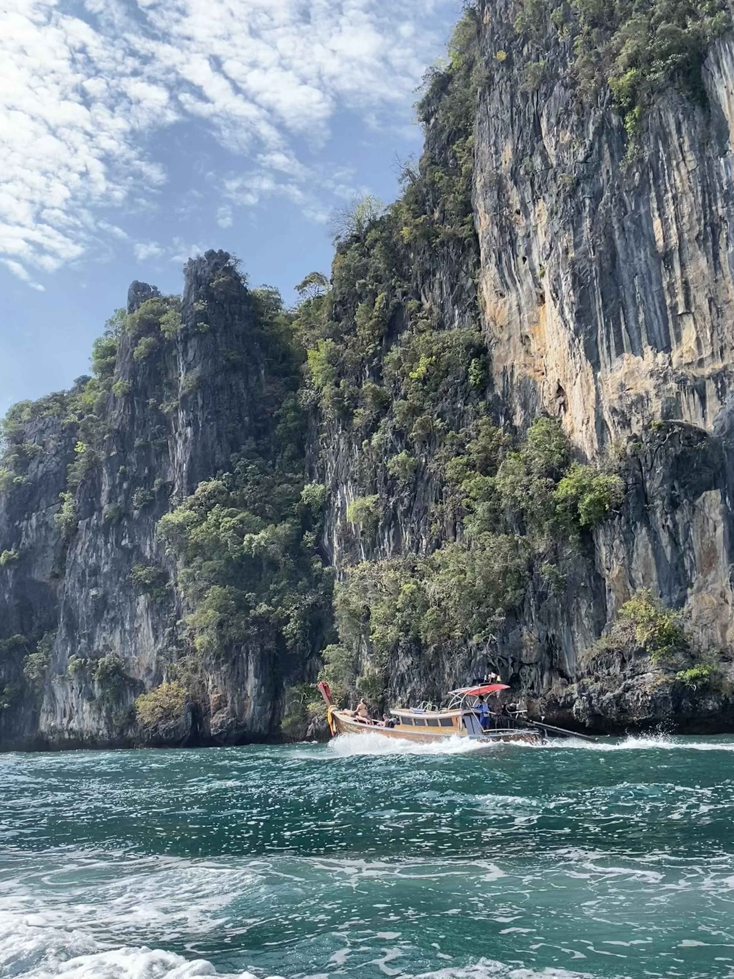 Longtail boat cruising beneath towering limestone cliffs in Krabi, Thailand