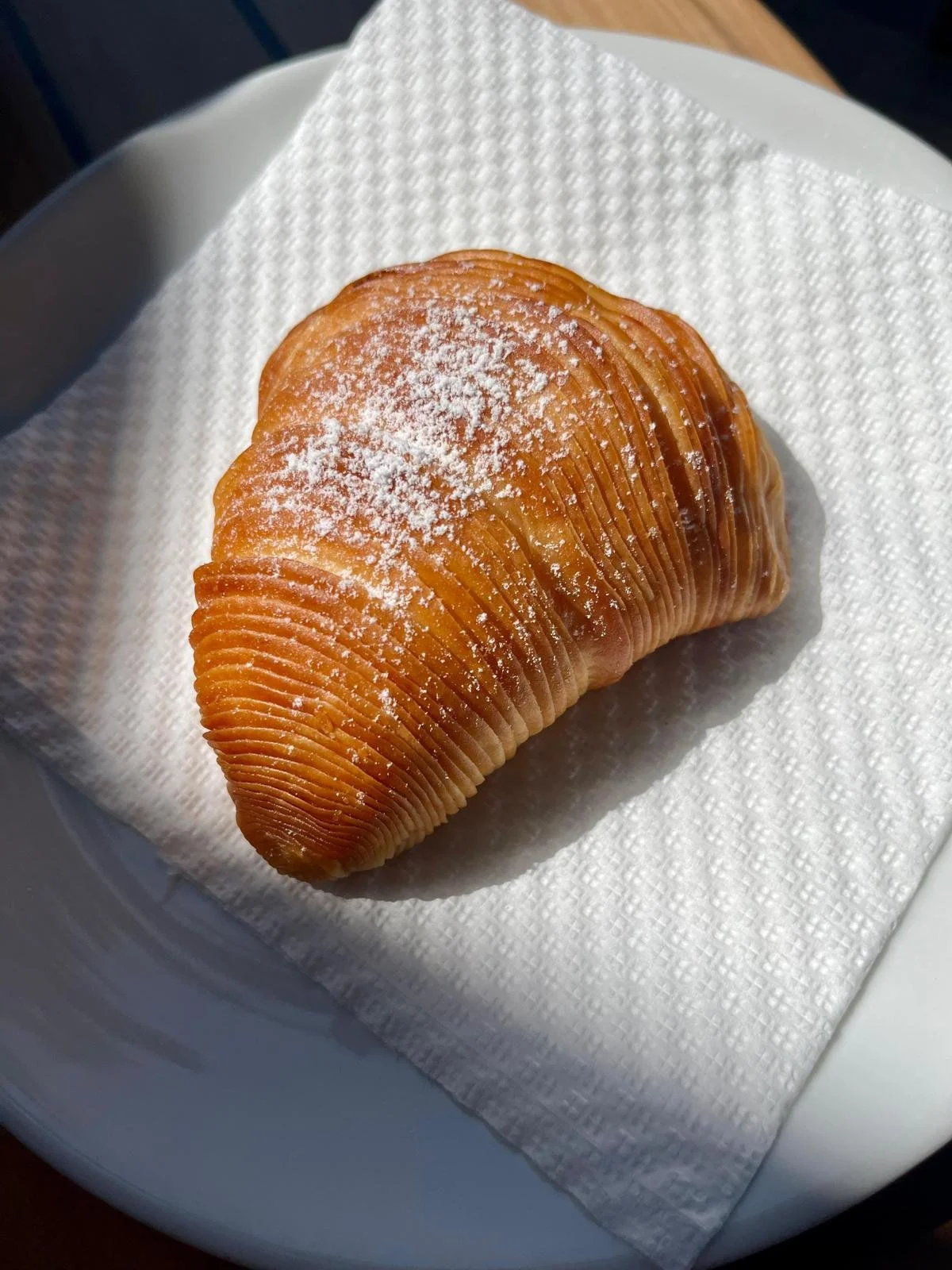 A freshly baked sfogliatella pastry with a golden-brown crust, dusted with powdered sugar, resting on a white napkin on a white plate.