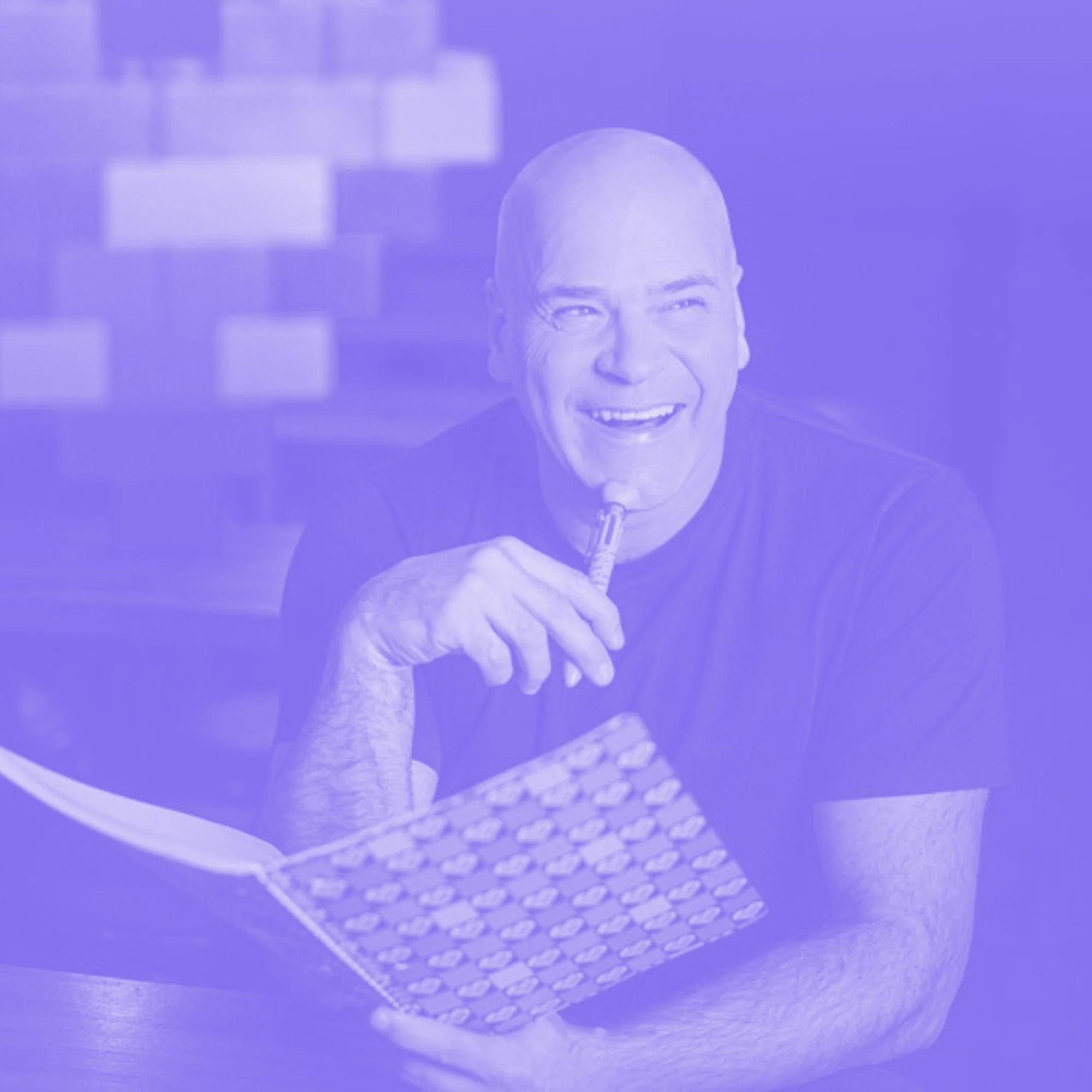 Un homme souriant assis à une table, tenant un livre avec un motif coloré, avec un cœur rempli de blocs de construction colorés en arrière-plan.