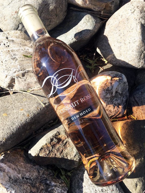 A clear glass bottle of rosé wine lying on rocks outdoors, labeled "CENSALT ROSÉ" and "DEN HOED."