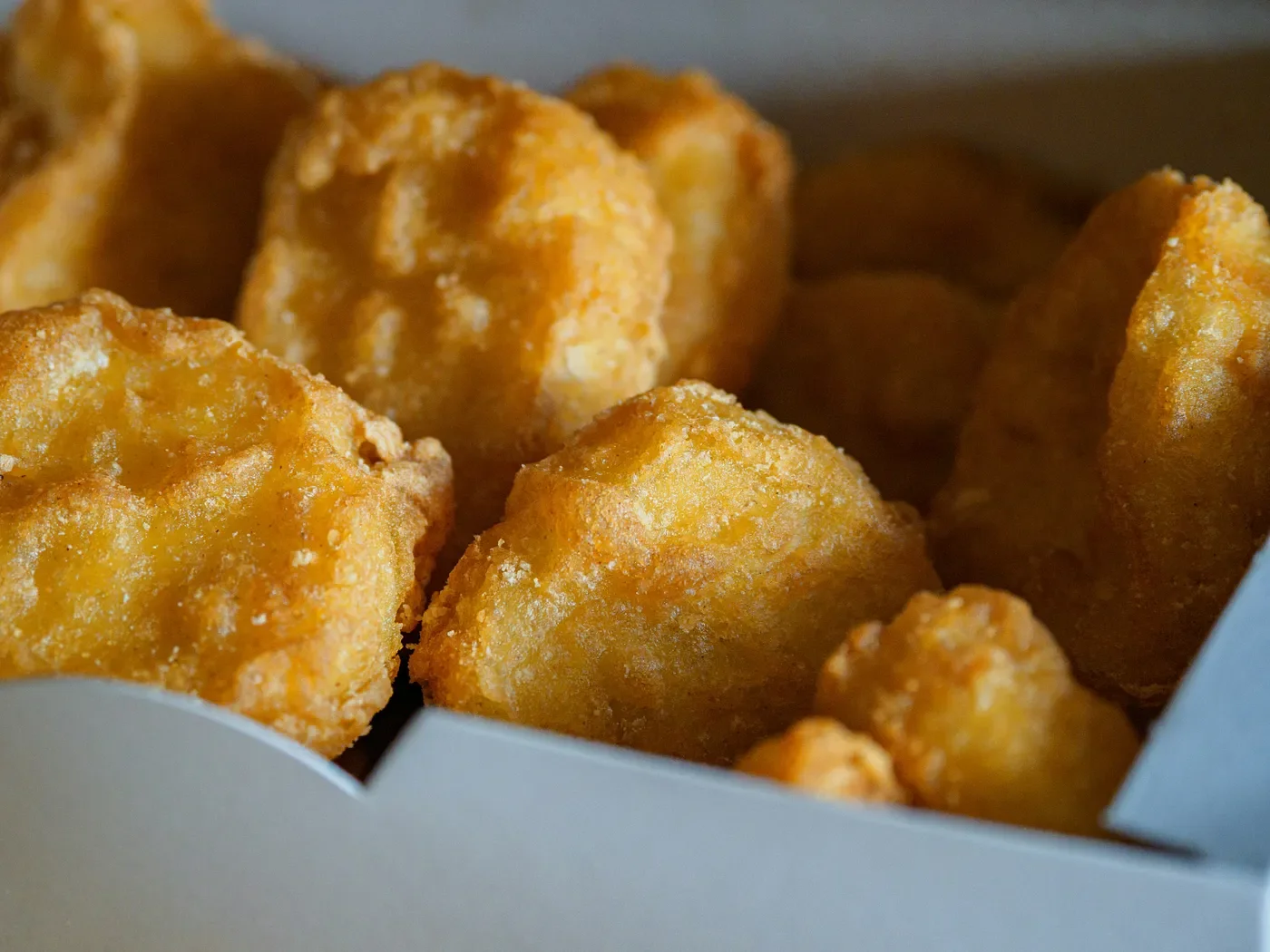 Close-up of fried chicken nuggets in a white takeout container.