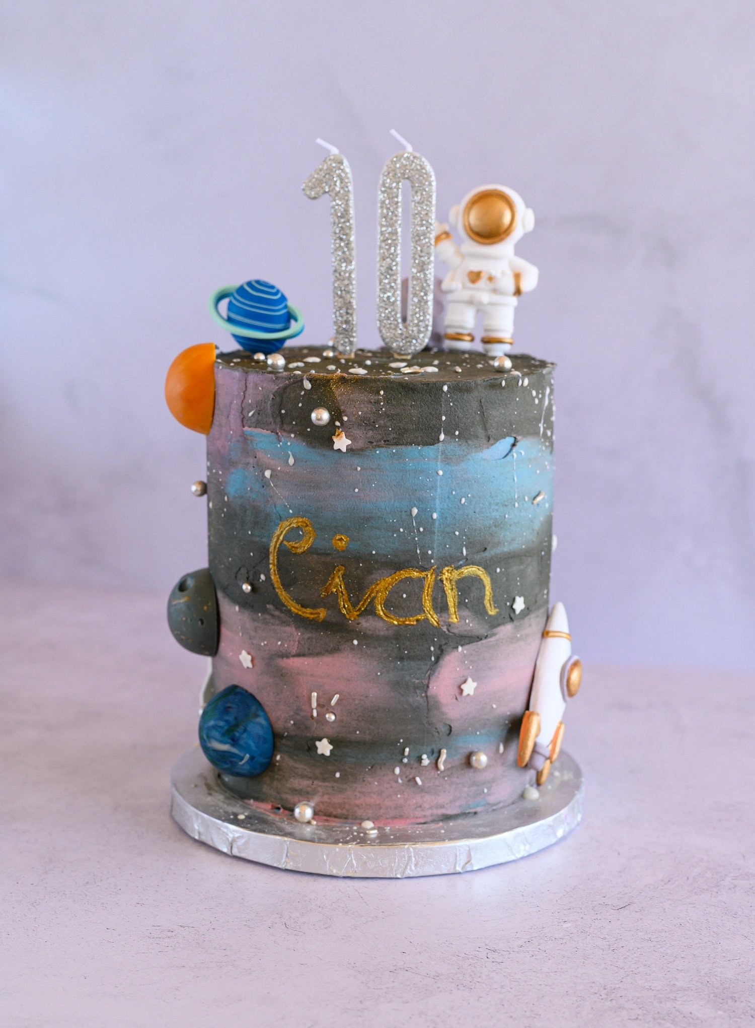 A space-themed cake decorated with solar system planets and an astronaut figure, with a glittery number 10 on top.