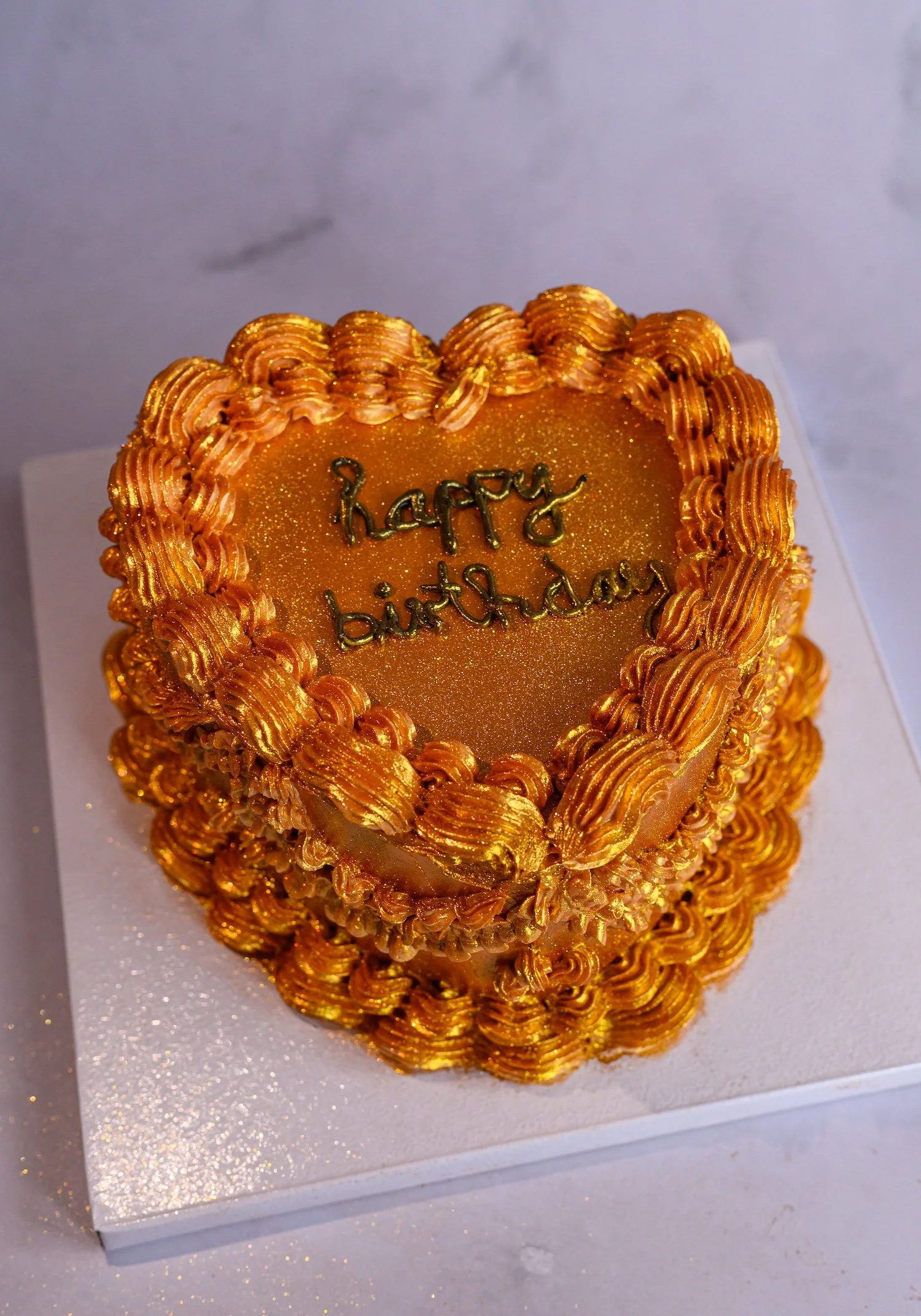 A gold birthday cake with decorative gold icing, featuring the words "happy birthday" written on top.