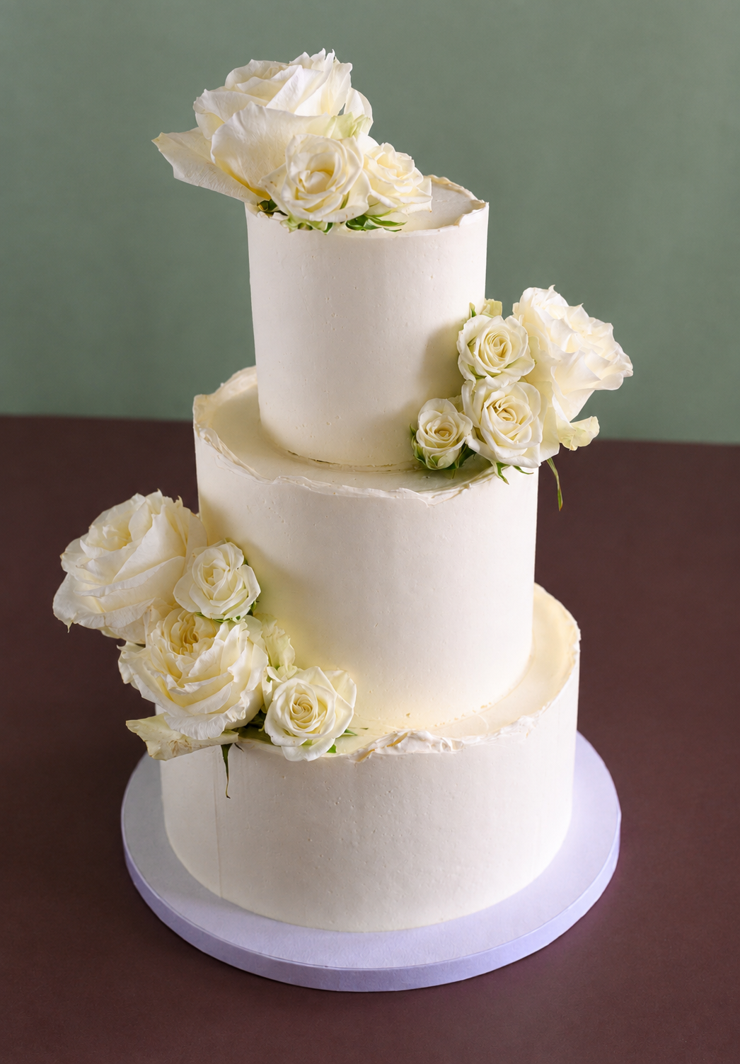 Three-tiered white wedding cake decorated with white roses and peonies.