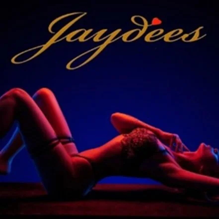 Poster for Jaydees showing a reclining woman in lingerie with a dark background and gold cursive text.