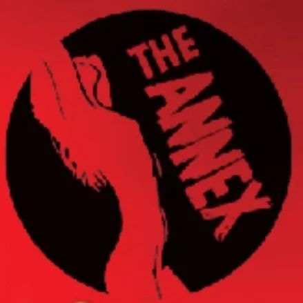 A red and black logo of the horror film 'The Ring,' featuring a stylized hand with a red nail and the text 'The Ring' inside a black circle.