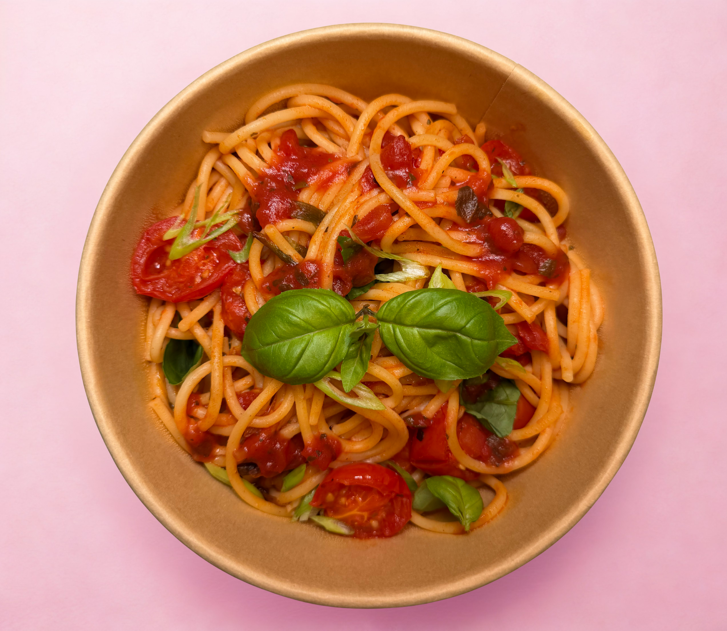 A bowl of spaghetti with tomato sauce, cherry tomatoes, olives and fresh basil leaves.