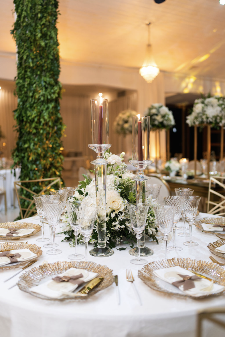Elegant banquet table decorated with white flowers, candles, and gold-rimmed glassware in a formal event setting