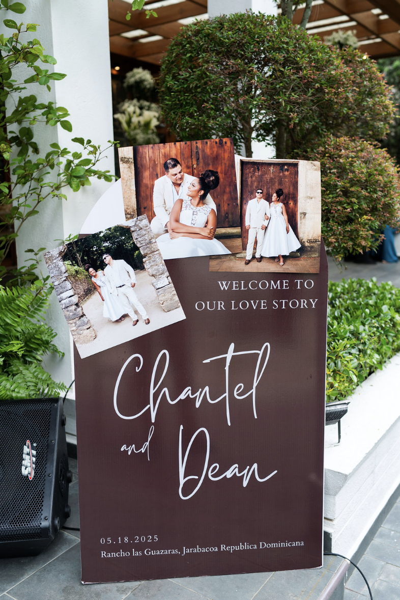 A wedding sign with photos of the couple, featuring images of a man and woman in white clothing, with a background of greenery. The sign reads "Welcome to our love story, Chante and Dean," and includes the date 05.18.2025 and location Rancho Las Guaz
