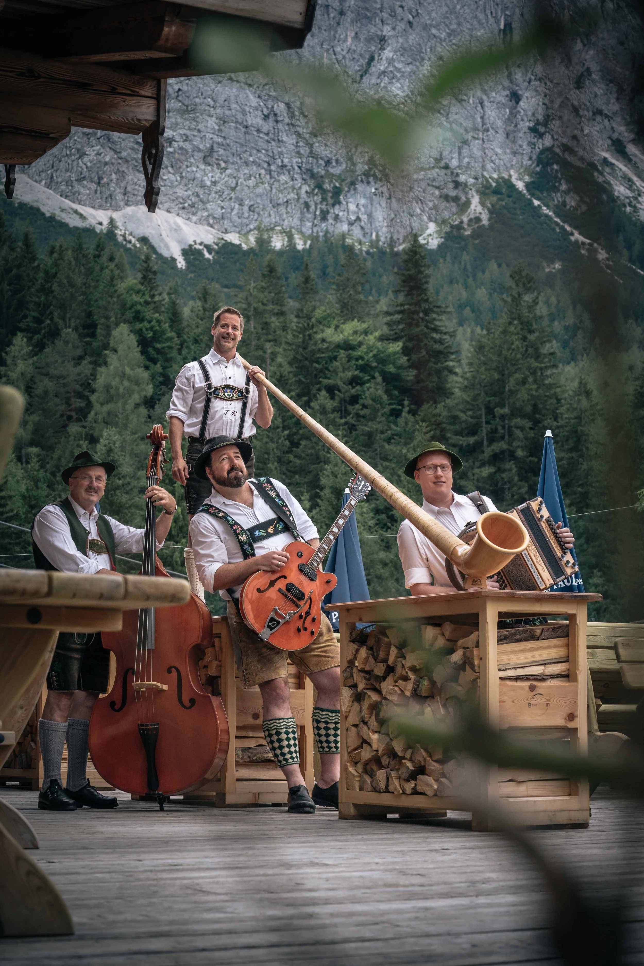 Gruppe von Musikern in traditionellen Trachten spielen in einer bergigen, bewaldeten Umgebung, mit Instrumenten wie Gitarre und Hackbrettern.