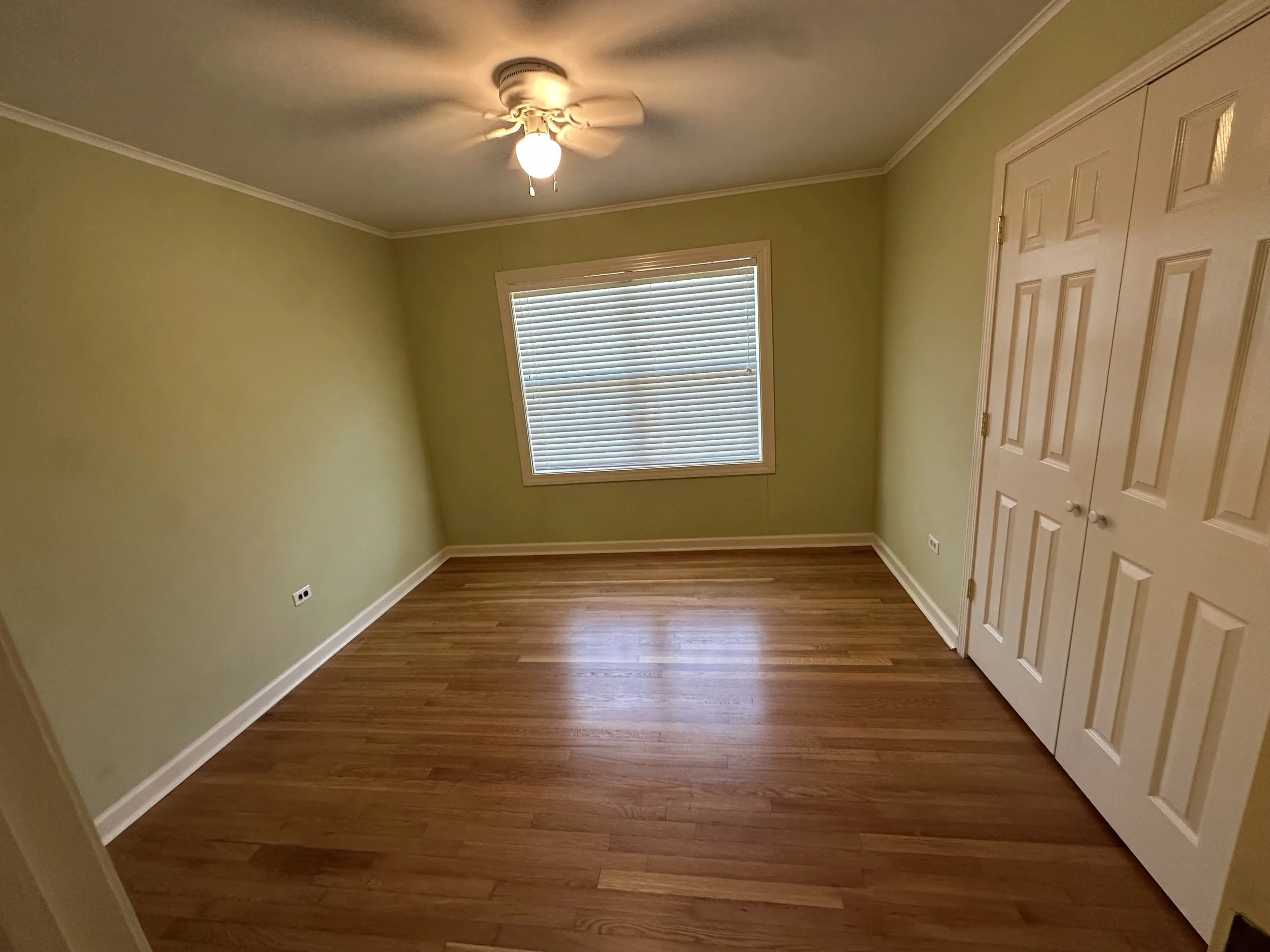 Empty bedroom with yellow walls, hardwood floor, a window with blinds, a ceiling fan with light, and a closet with double doors.
