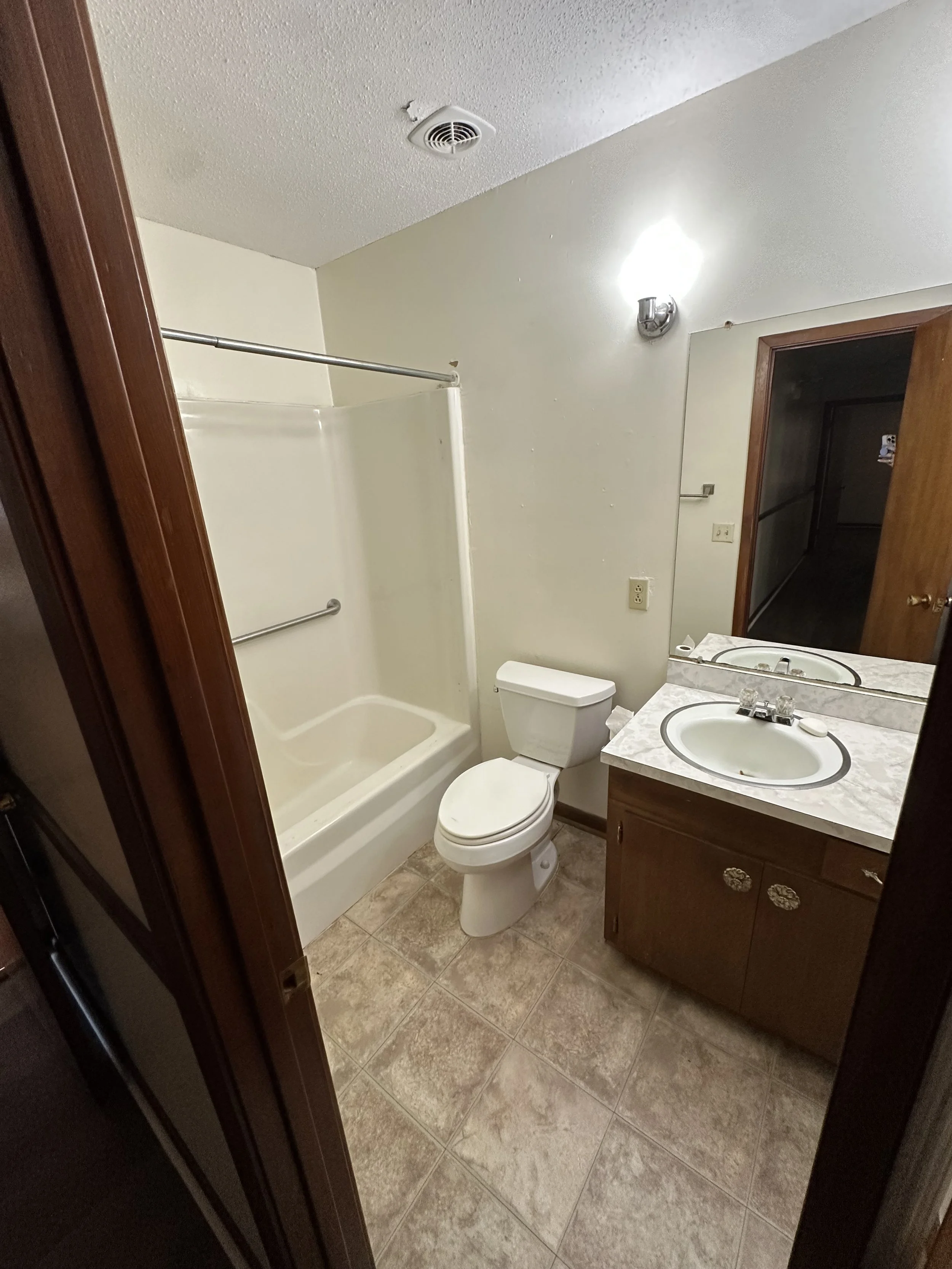 Small bathroom featuring a bathtub with a shower curtain rod, toilet, vanity with a sink and mirror, and a wall light fixture.