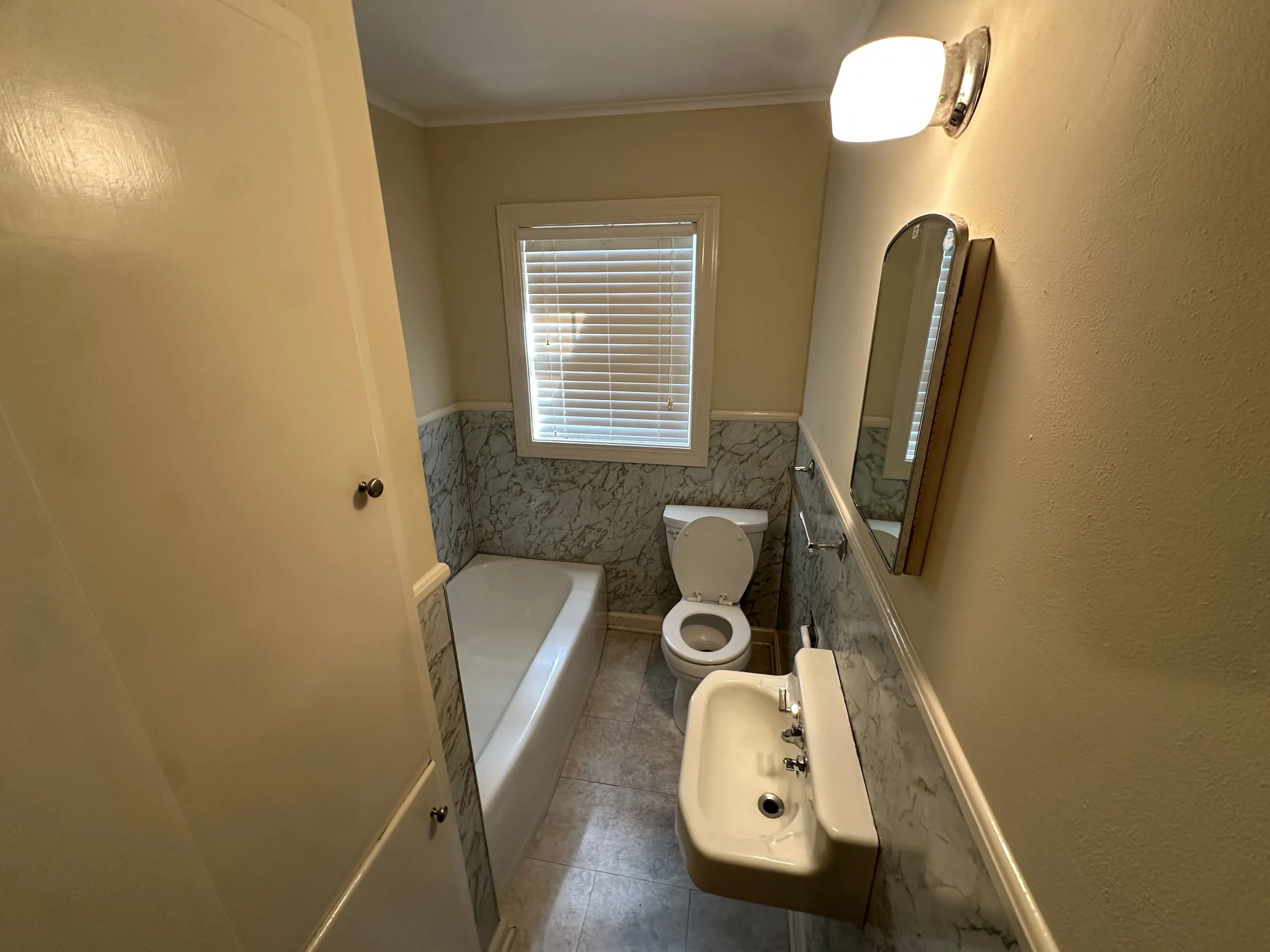 Small bathroom with a window, bathtub, toilet, and sink, featuring a wall-mounted mirror.