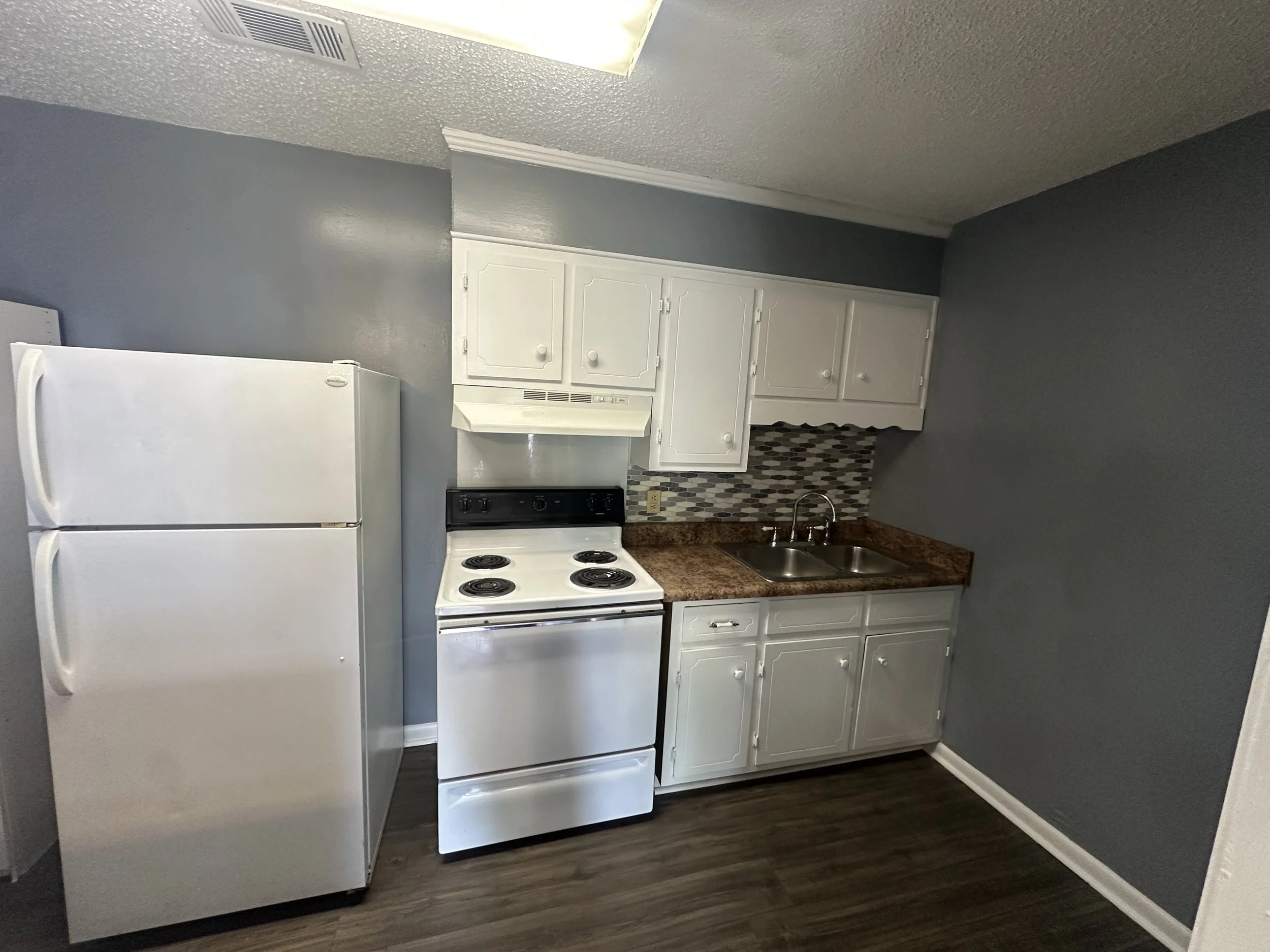 Small kitchen with white refrigerator, white stove, white cabinets, brown countertops, gray walls, and wood-look flooring.