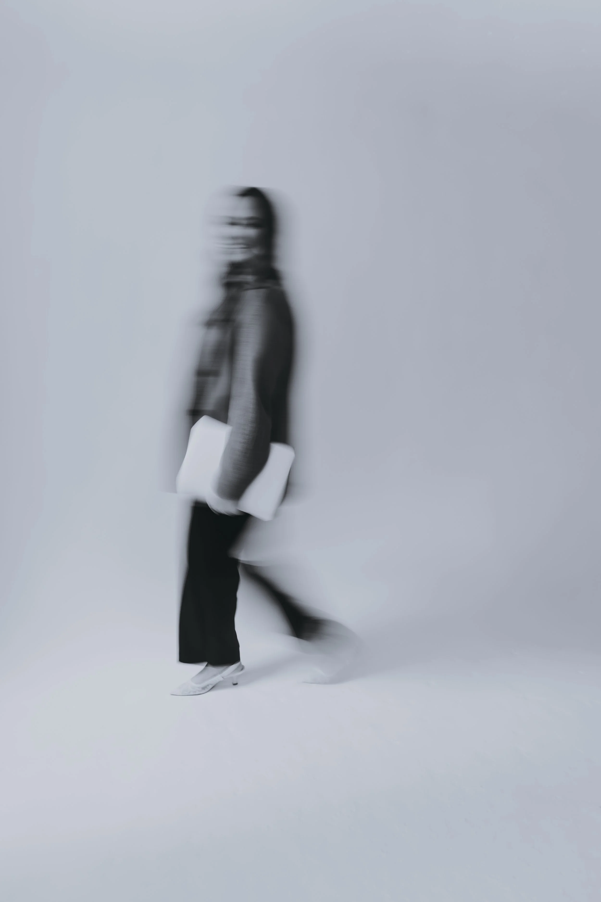 A person carrying a laptop in each hand, walking with a blurred background and motion blur effect.