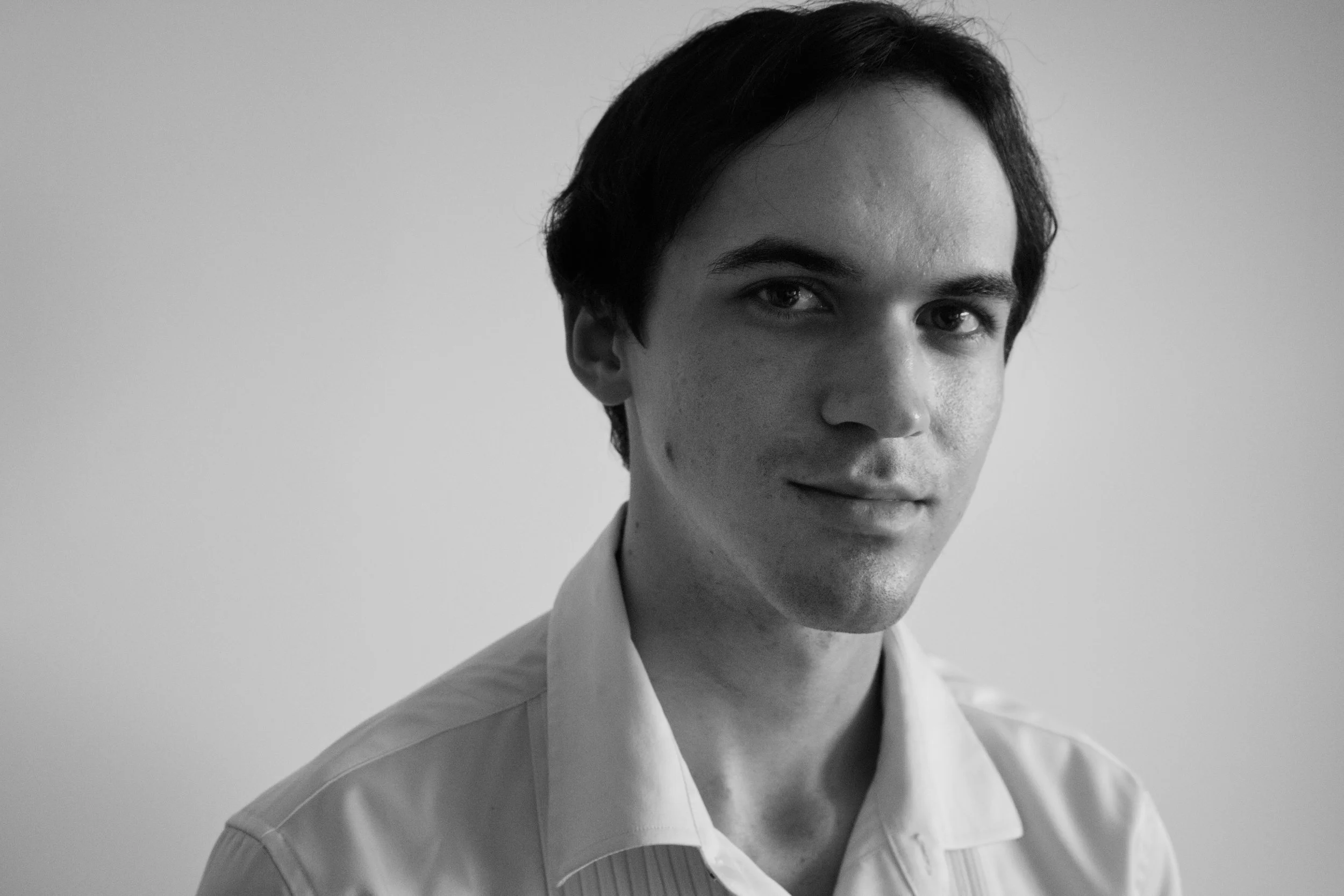 Close-up black and white portrait of Christopher Lutsker with dark hair, wearing a collared shirt, partially smiling against a plain background.
