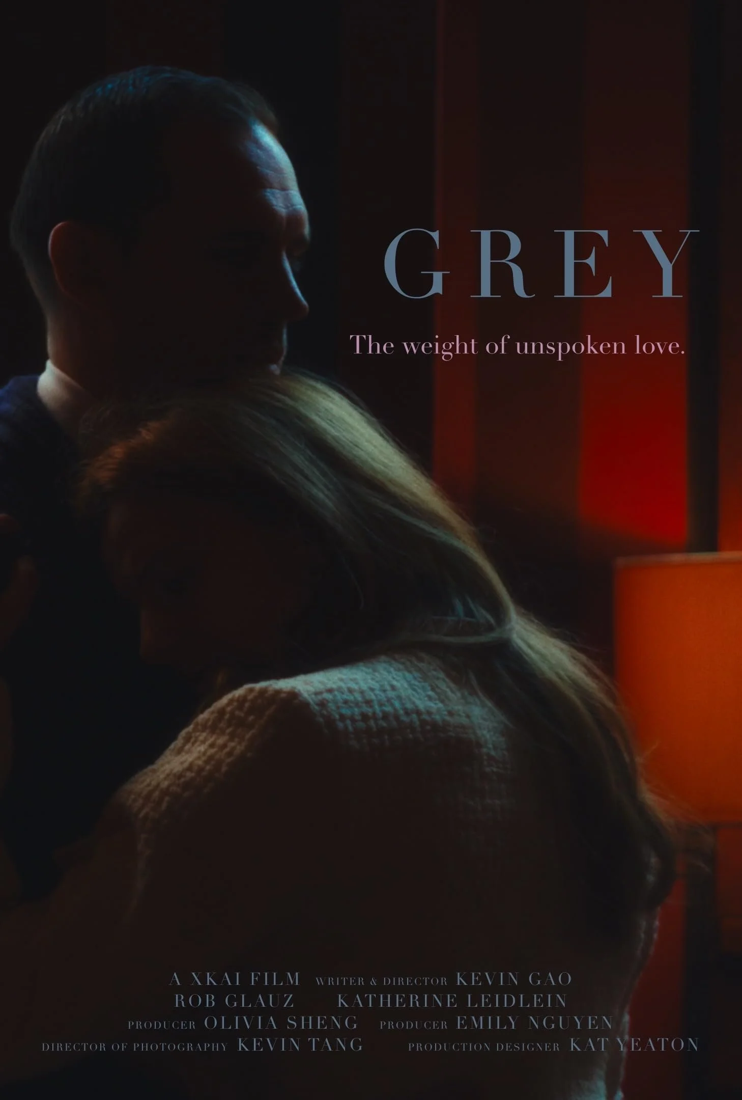 Dark side profile of a man and a woman embracing in front of a red-orange background with the title 'GREY' and the tagline 'The weight of unspoken love' written on it. Credits at the bottom for the film.