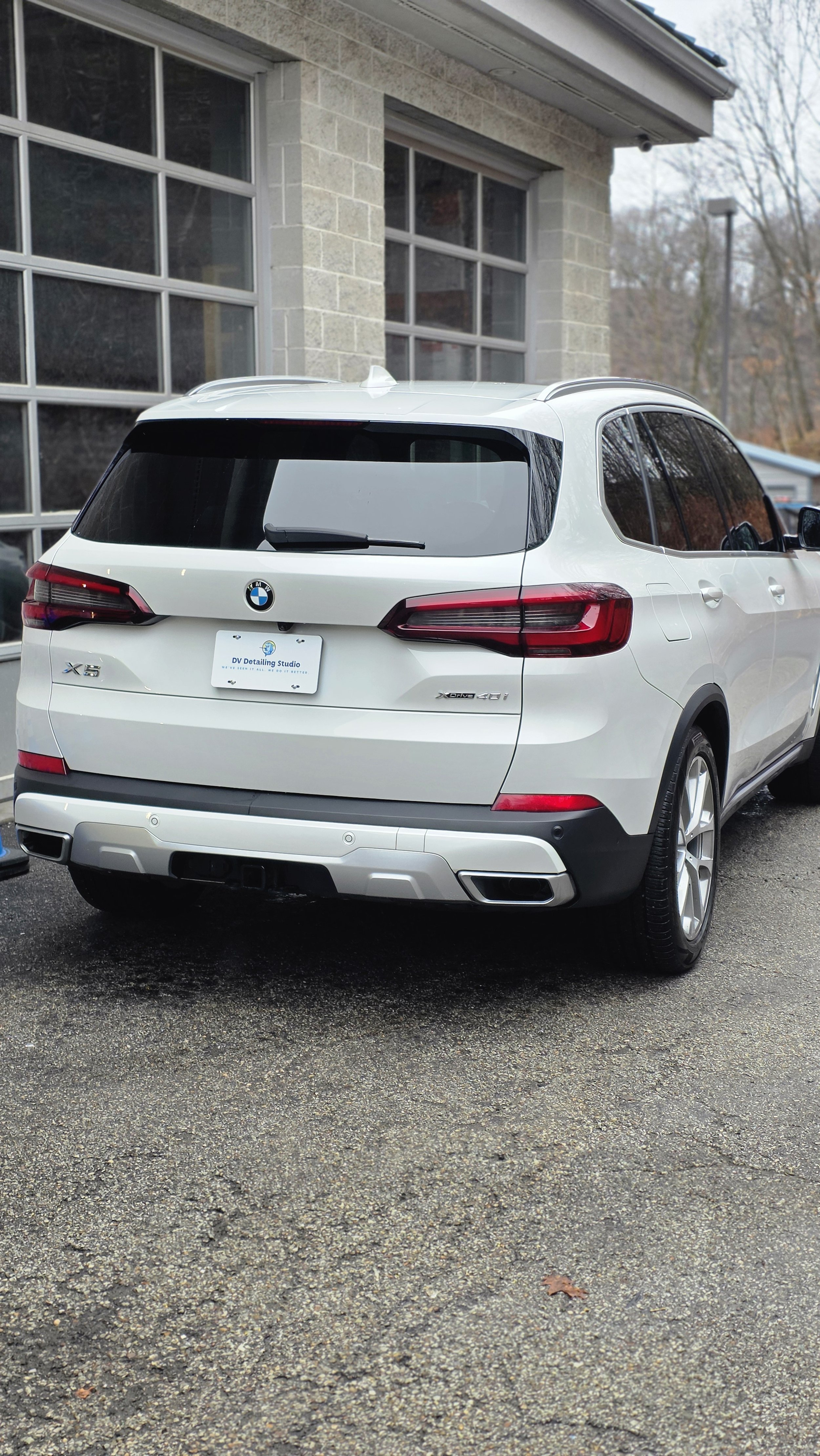 Rear view of a white BMW X5 parked on a paved driveway in front of a gray brick building.