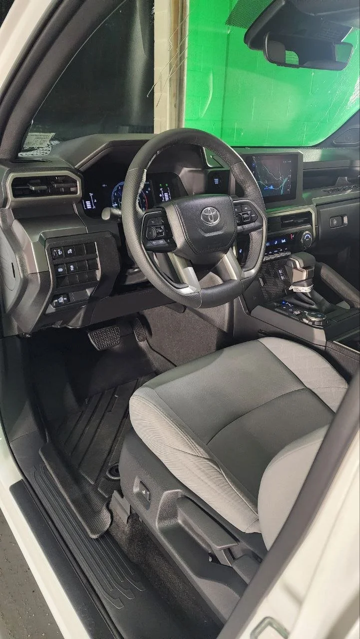 Inside the driver's side of a Toyota vehicle, showing the steering wheel, dashboard, center console, and front seat.