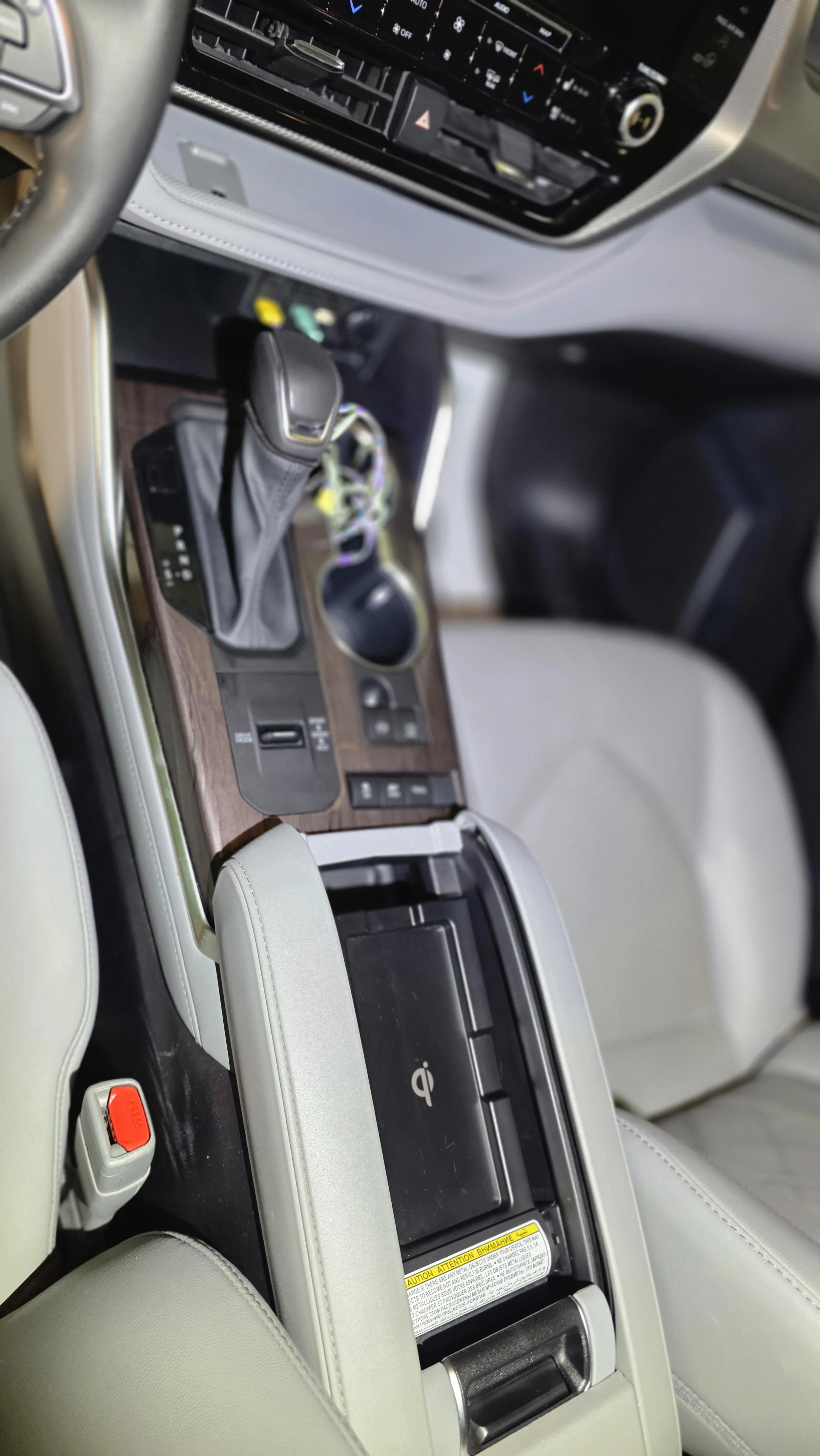Interior of a vehicle showing the center console with a gear shift, cup holder, electronic parking brake switch, and a closed wireless charging pad. The dashboard with controls and an infotainment system are partly visible.