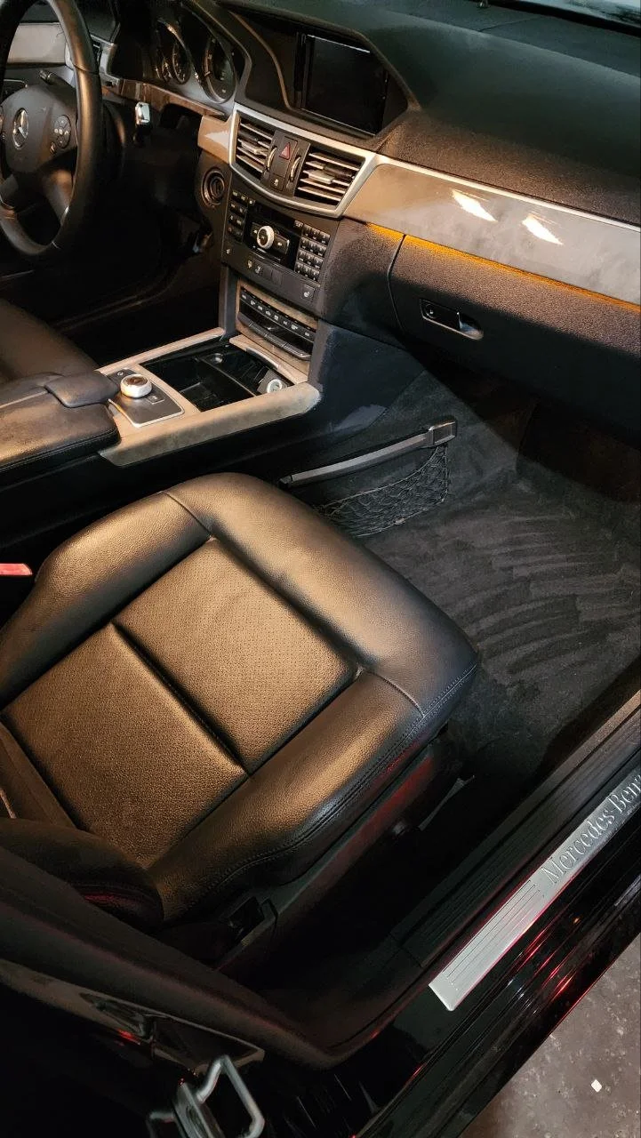 Interior of a Mercedes-Benz vehicle showing the dashboard, center console, driver's seat, and part of the door sill with the Mercedes-Benz logo.