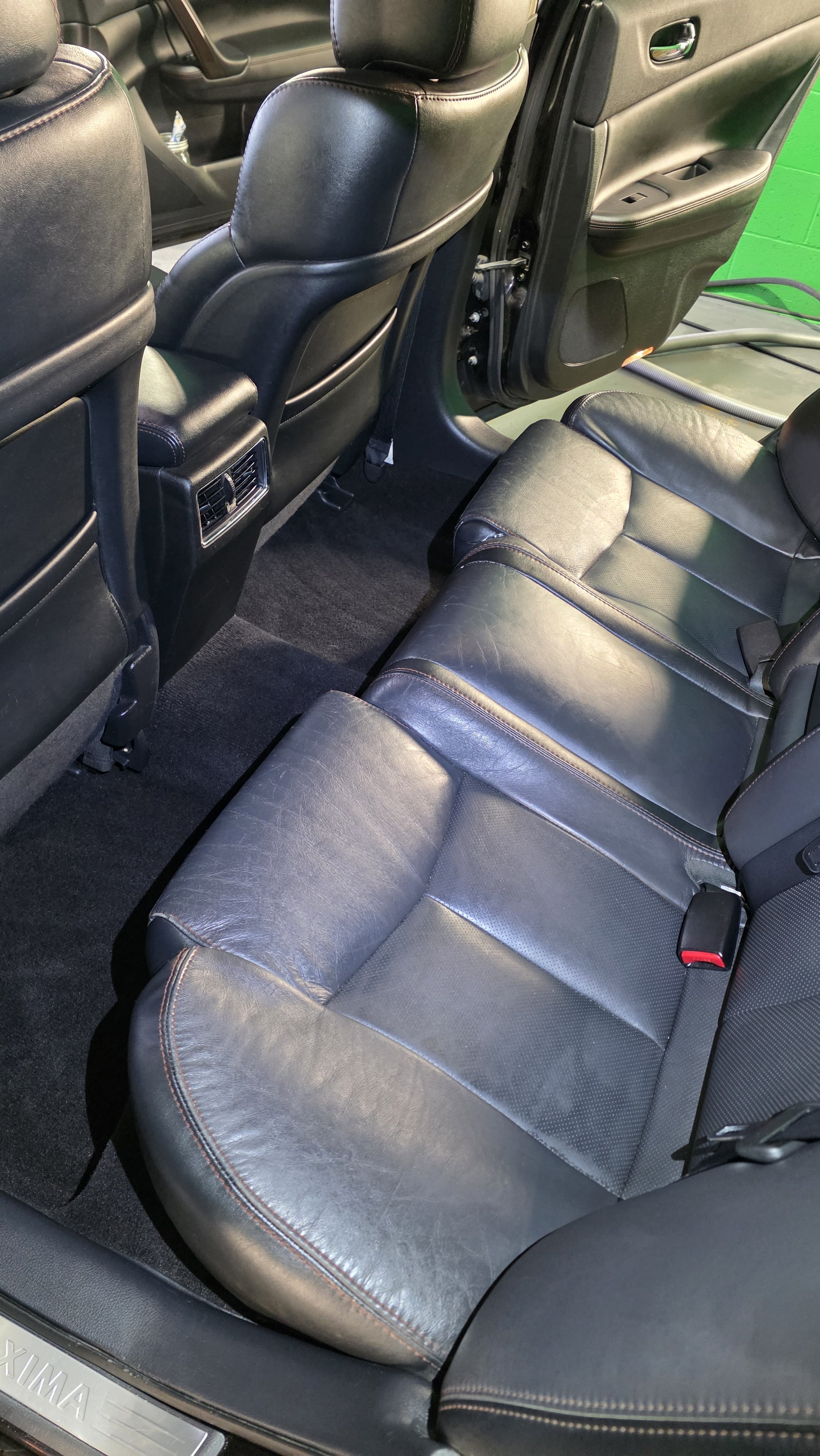 The backseat interior of a car with black leather seats and a black carpet floor, showing the rear passenger seats and part of the front seat backs.