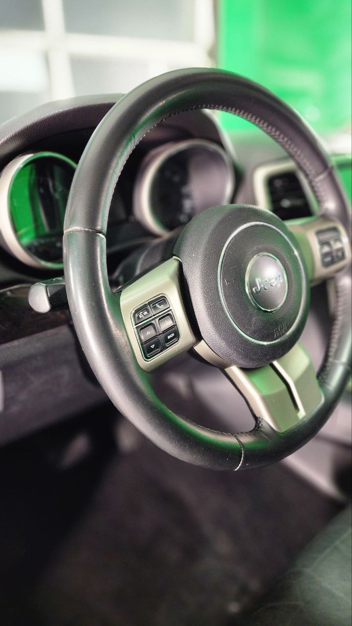 Close-up of a car's steering wheel with control buttons, Jeep logo in the center, and dashboard gauges in the background.