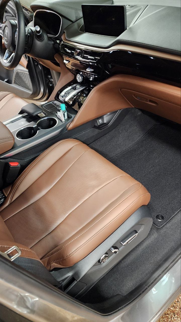 Interior of a car showing a steering wheel, dashboard, center console with cup holders, brown leather seats, and a display screen on the dashboard.