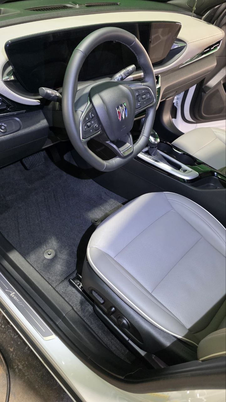 Inside view of the driver's seat of a modern electric car with a digital dashboard and steering wheel featuring control buttons.