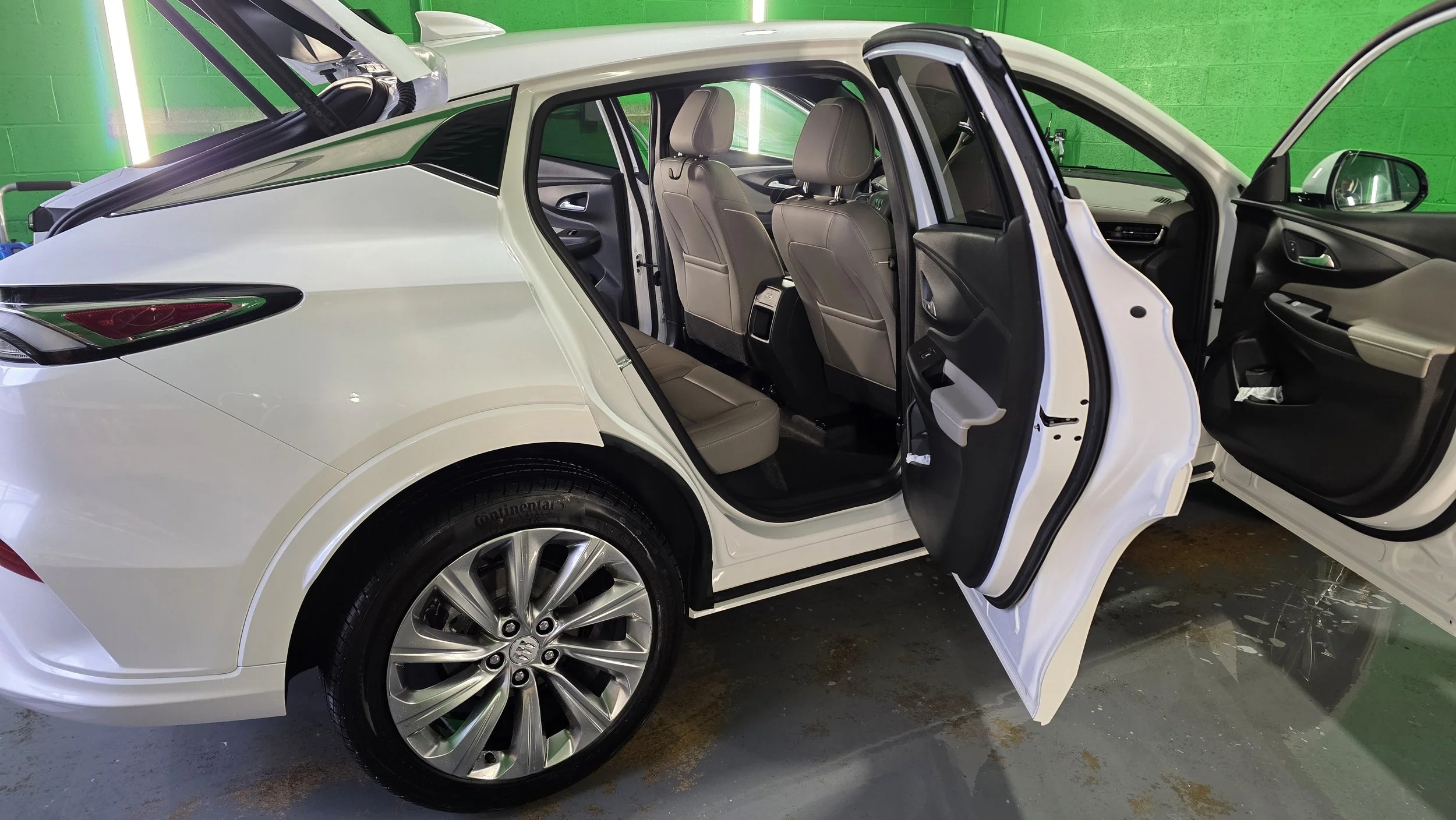 White sedan car with open doors showing beige interior and front seats, parked indoors against a green wall.