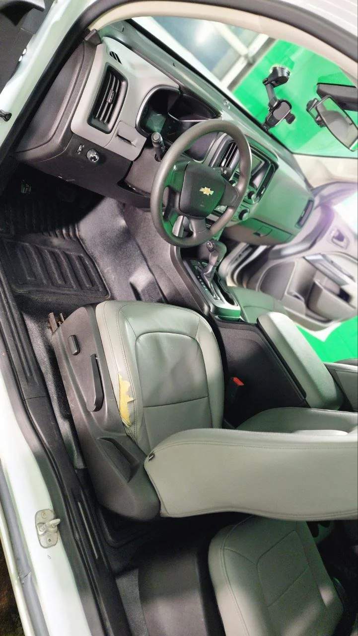 Interior of a Chevrolet vehicle showing the dashboard, steering wheel, center console, and front seats, with the driver's seat damaged and peeling.