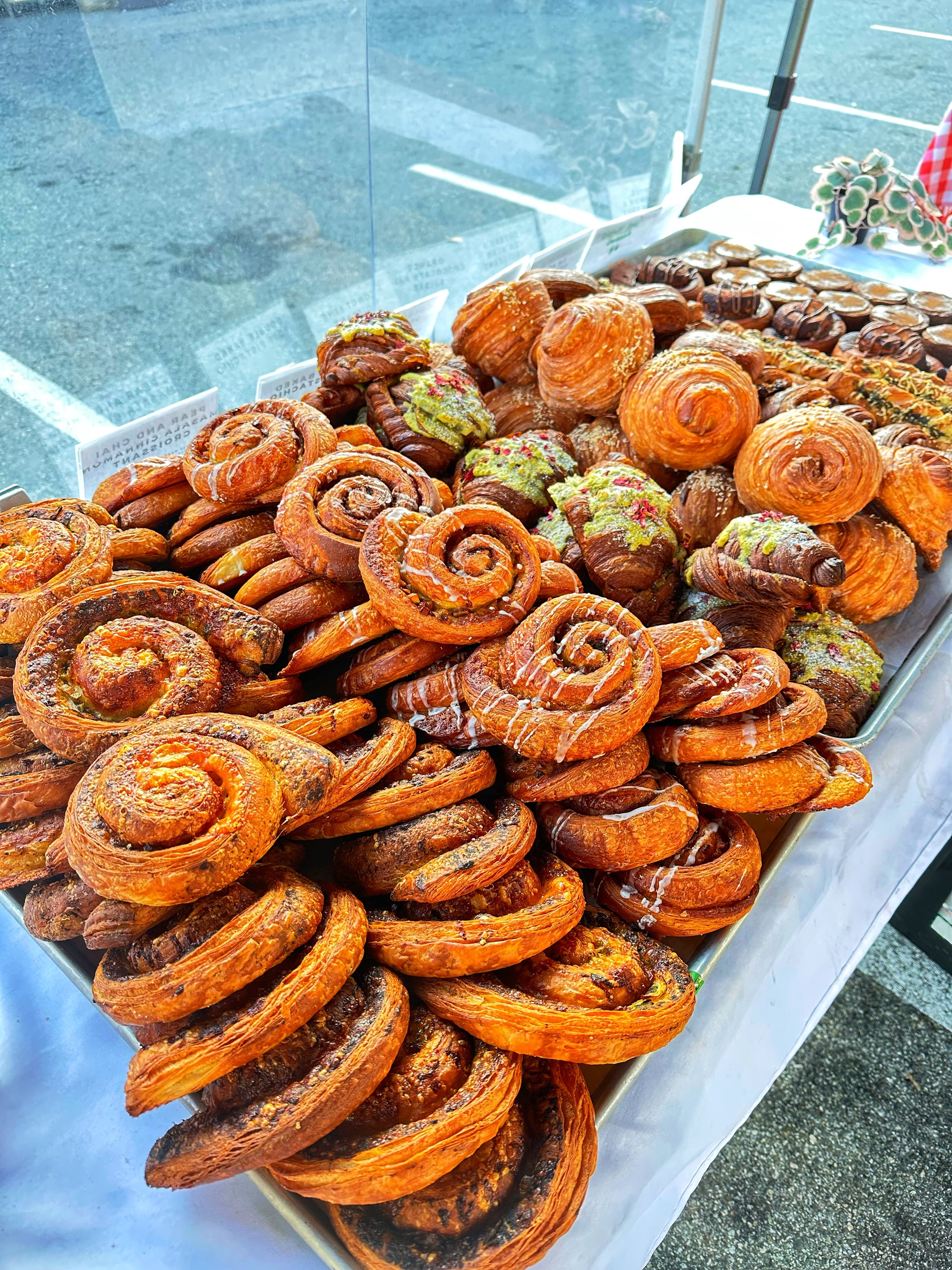 A tray of assorted baked pastries, including cinnamon rolls and Danish pastries, displayed on a table outdoors.