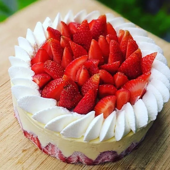 Round strawberry cake topped with sliced strawberries and whipped cream, with a white icing border.