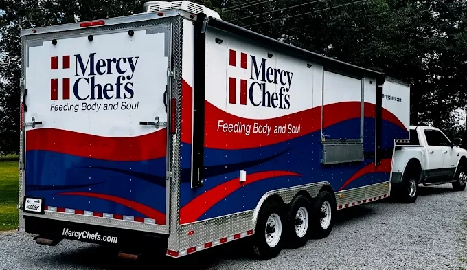 A food truck with a white cab and a large, colorful body featuring red, blue, and white design elements. The truck displays the Mercury Chefs logo and the slogan "Feeding Body and Soul" on the side.