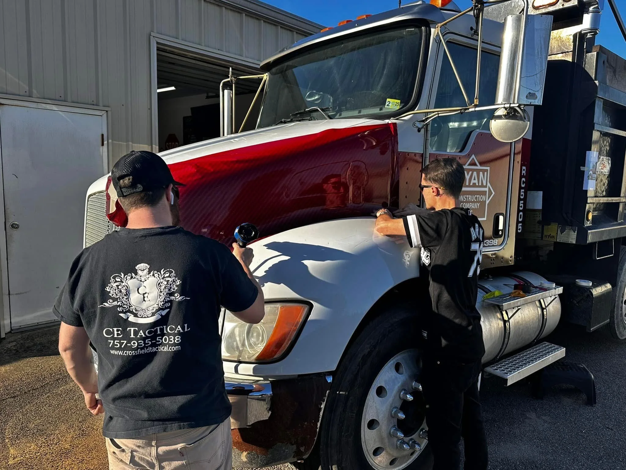 Two men working on a semi-truck outside a garage.