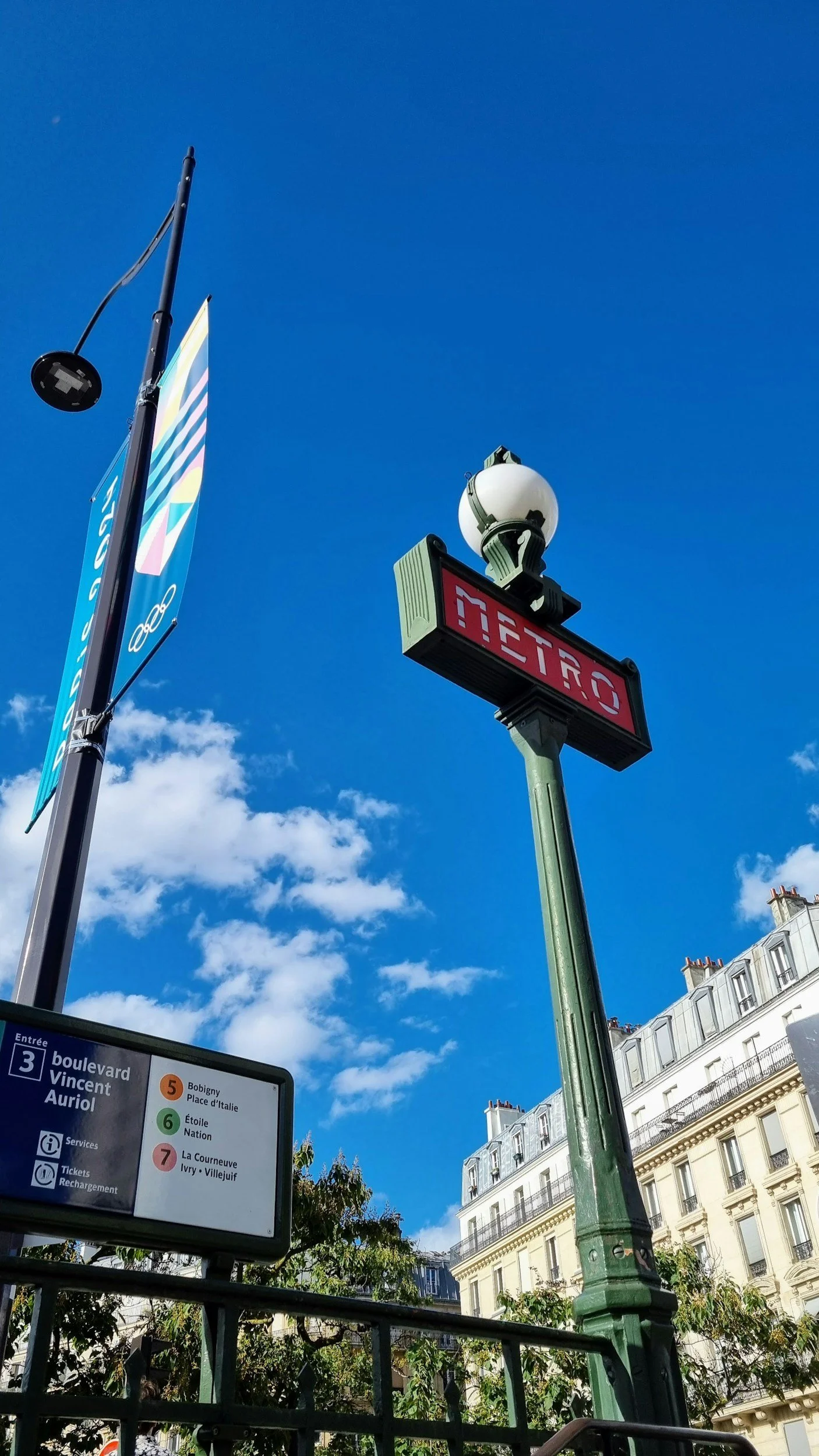 Paris Metro entrance with route information and buildings along a city street