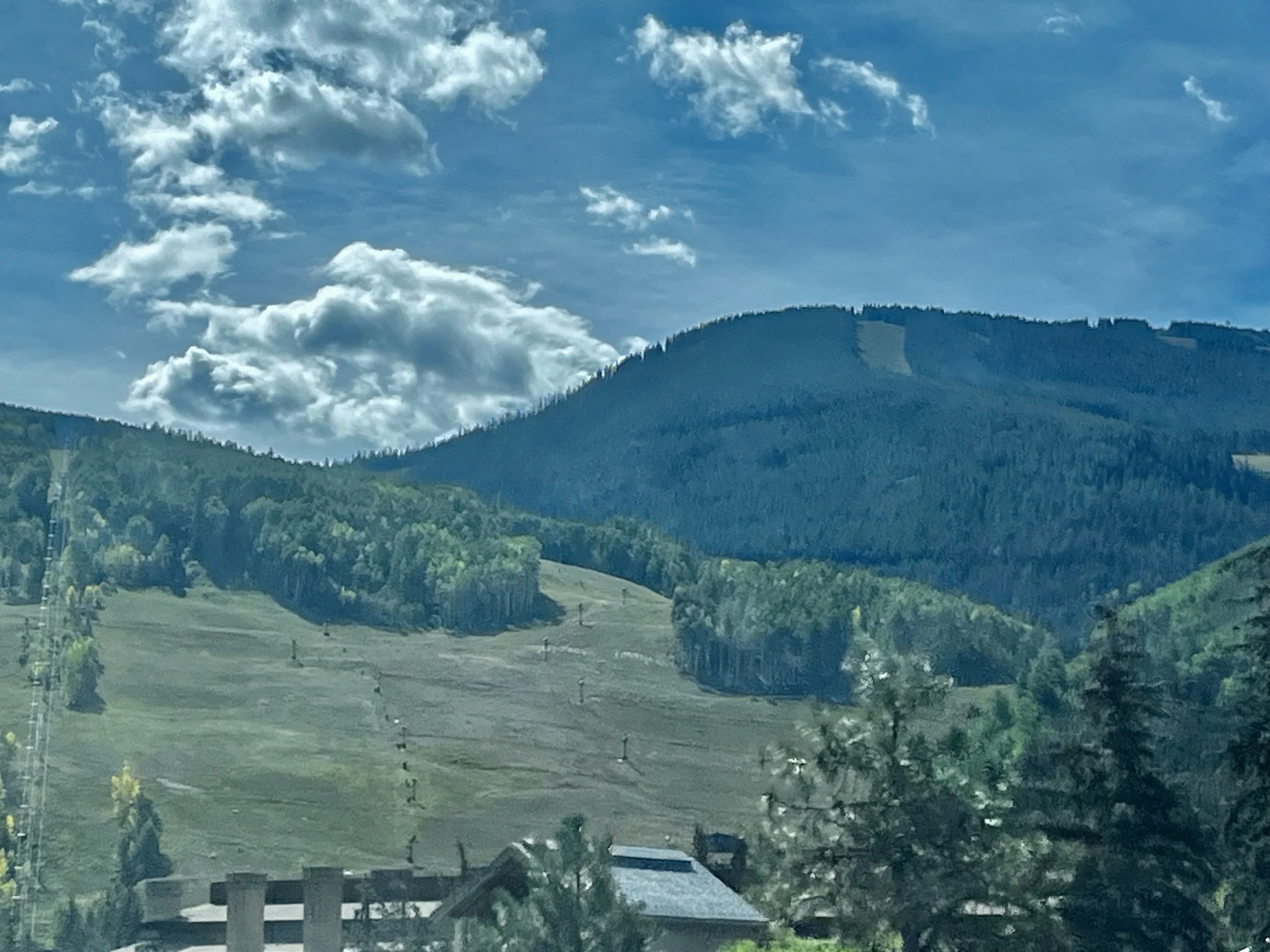 Mountain slopes and trees at Copper Mountain, Colorado, beneath a partly cloudy blue sky.